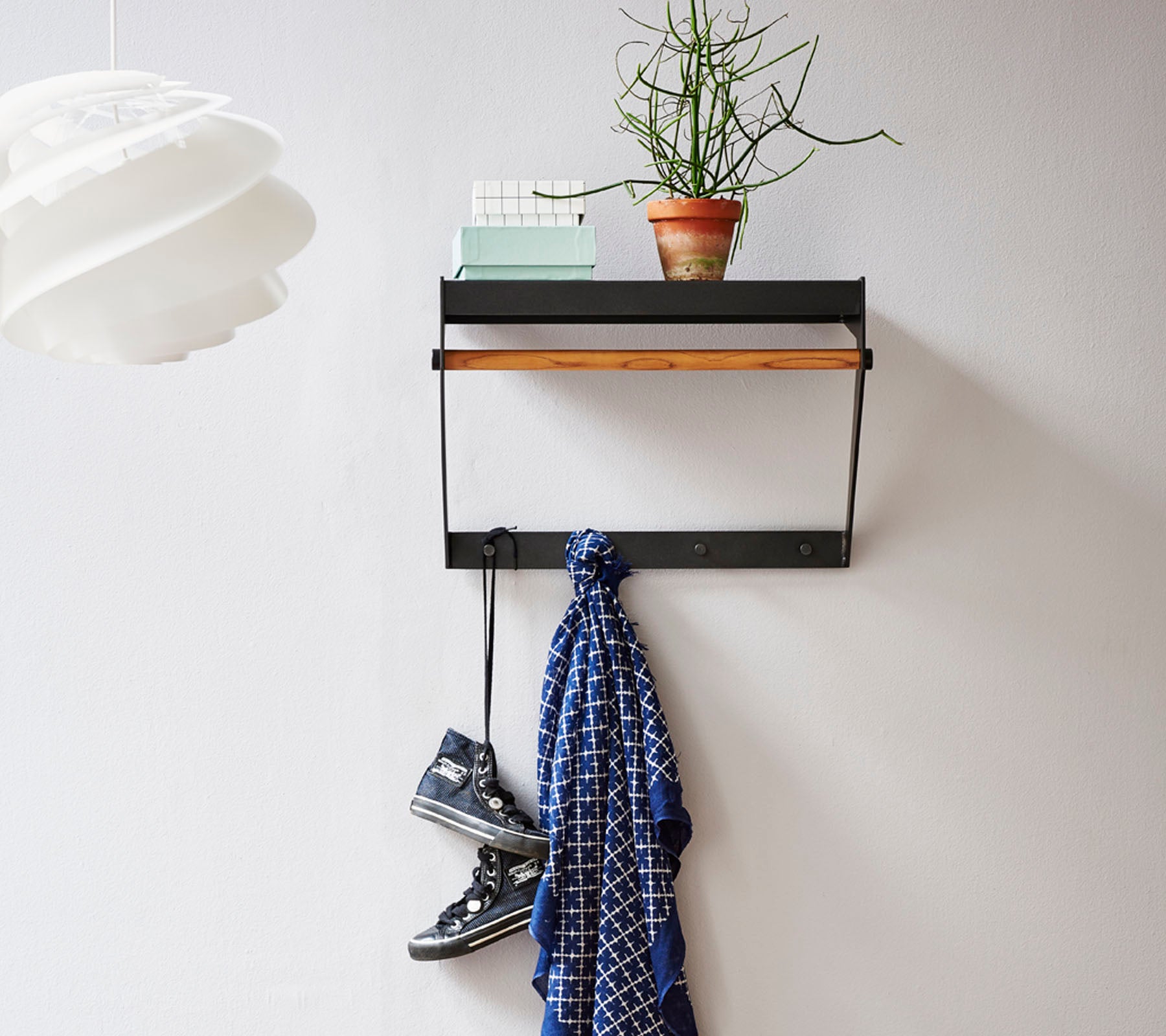 Estante de pared con una parte superior de madera, que presenta una pequeña planta, una bufanda colgando abajo y un par de zapatos en el suelo.