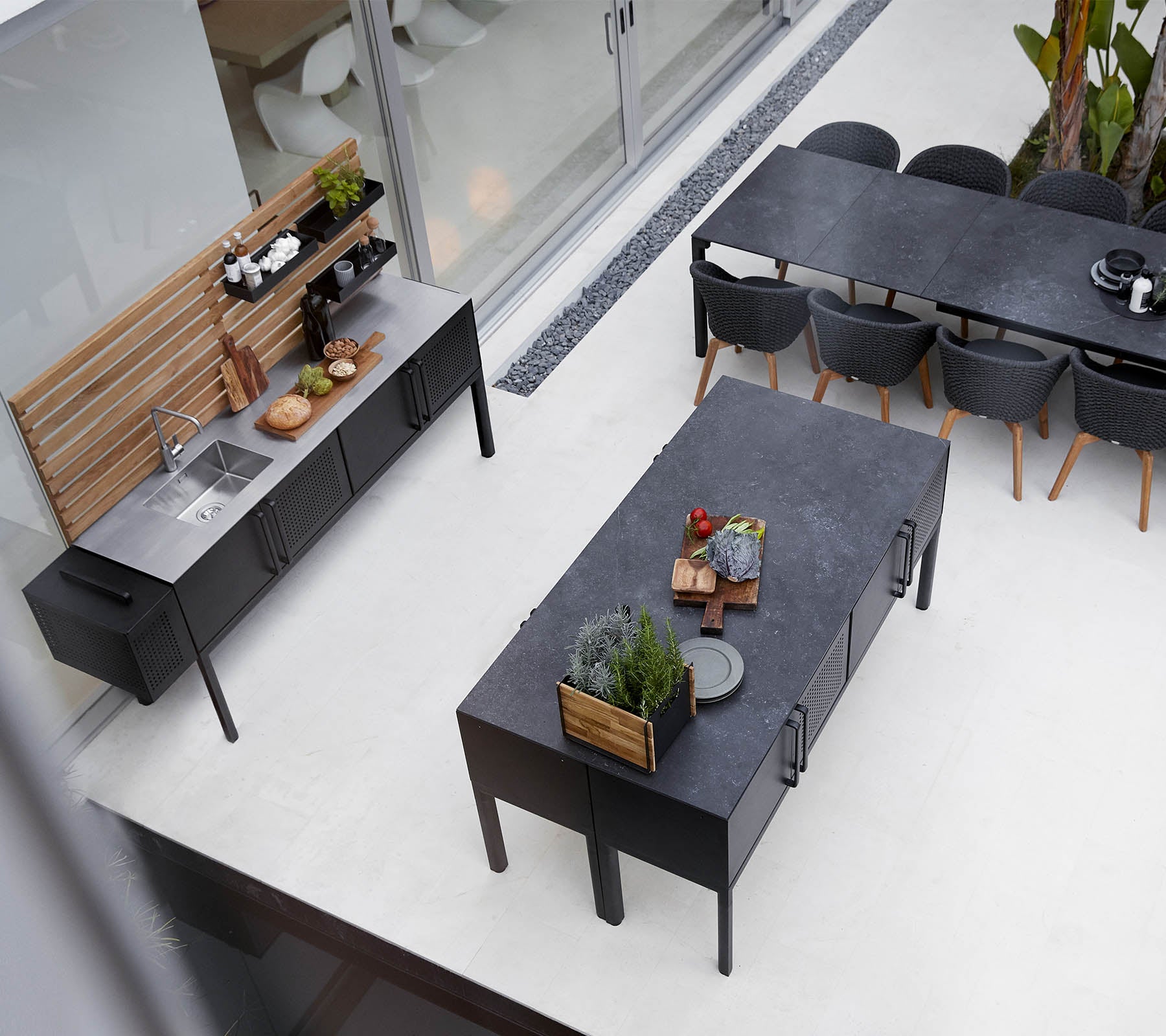 Configuración moderna de cocina al aire libre con una encimera elegante, una mesa de comedor espaciosa y un arreglo de asientos elegante con plantas y elementos decorativos.