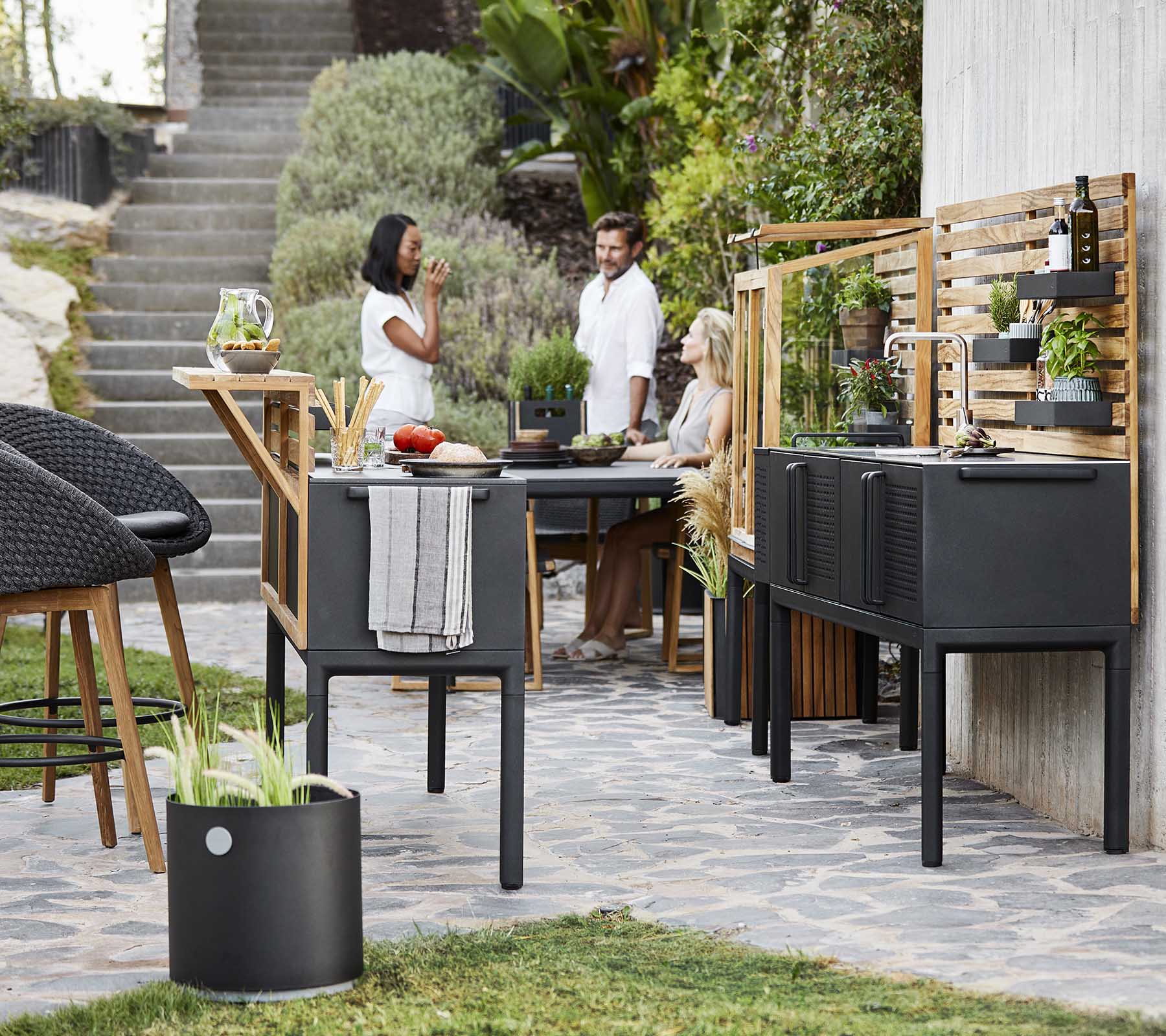 Un área moderna de comedor al aire libre con muebles negros elegantes, vegetación y personas disfrutando de una comida juntos.