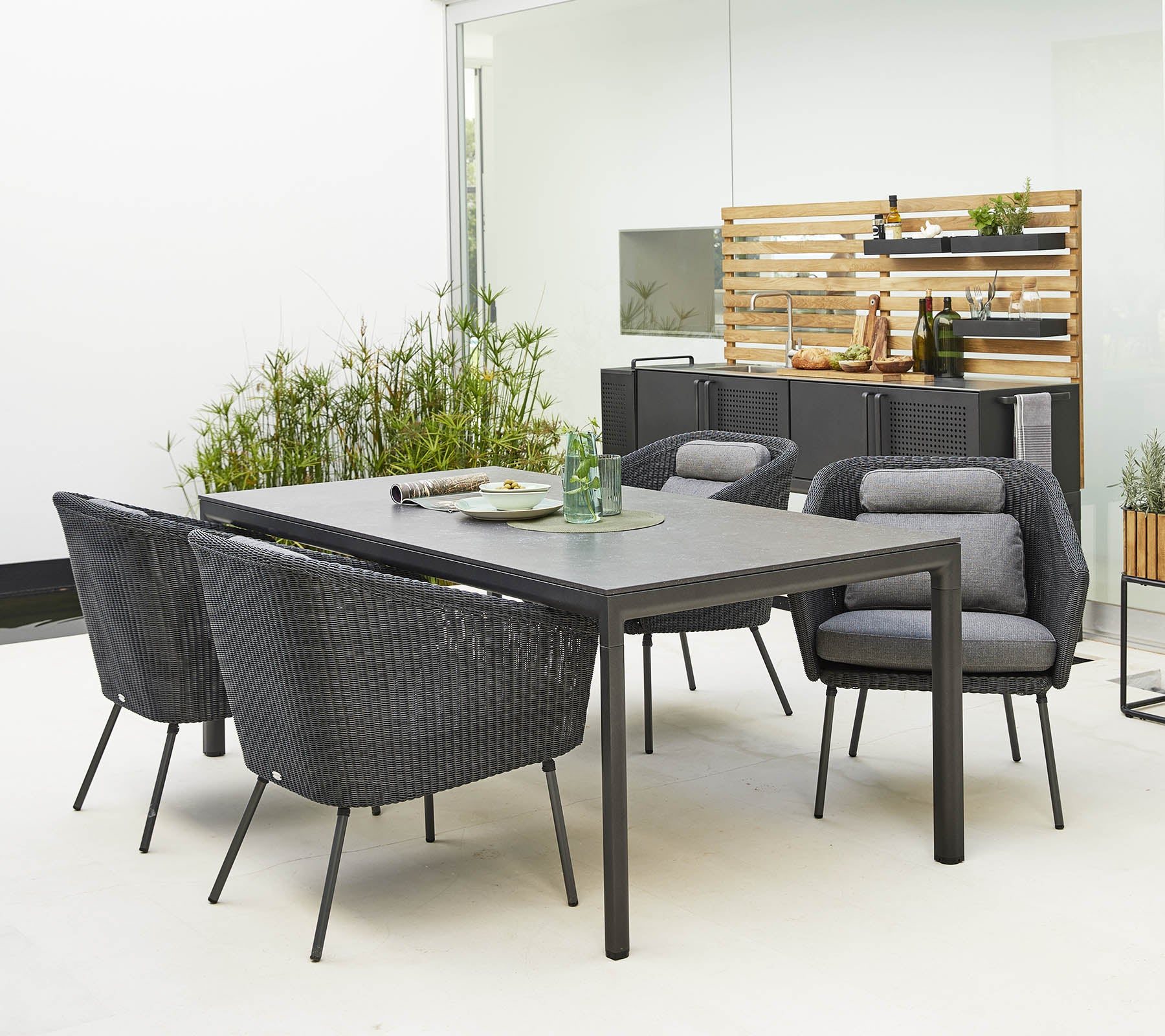 Conjunto de comedor al aire libre elegante que presenta una mesa elegante y cómodas sillas modernas rodeadas de vegetación decorativa.