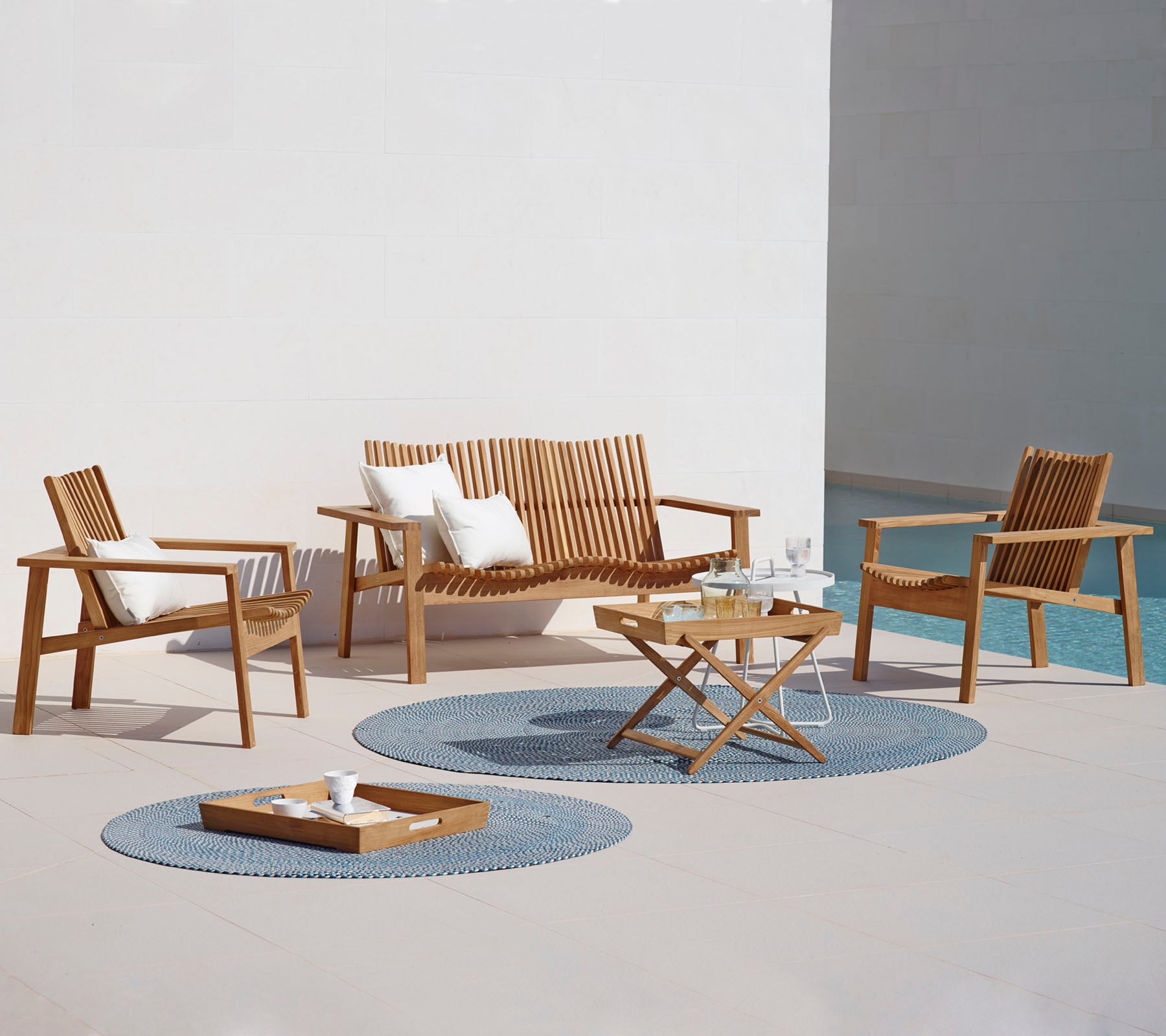 Un elegante disposición de asientos al aire libre que incluye un sofá, dos sillas, una mesa de café y alfombras decorativas. Ideal para relajarse.