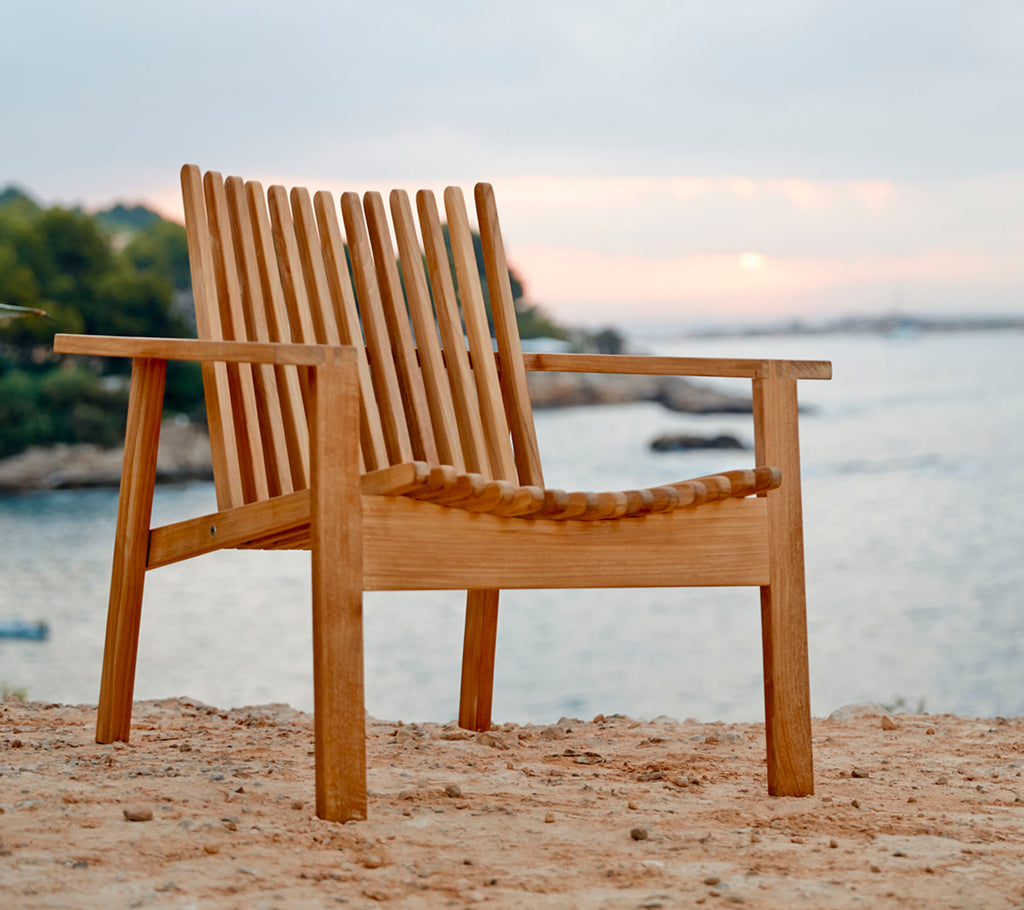 Una silla de madera con respaldo y asiento de listones, situada cerca del agua, mostrando un entorno natural y sereno.