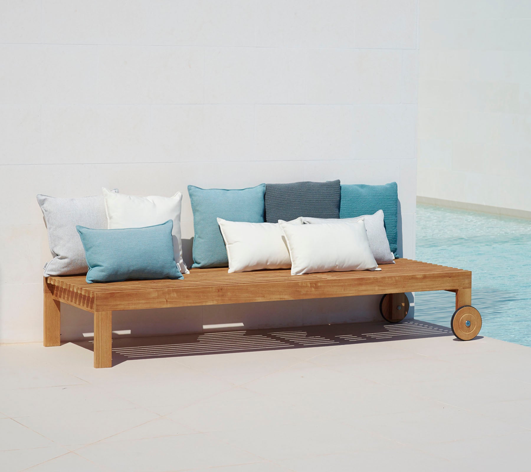 Sofá de madera con un diseño simple, con cojines en tonos de azul y blanco, colocado al lado de una piscina.