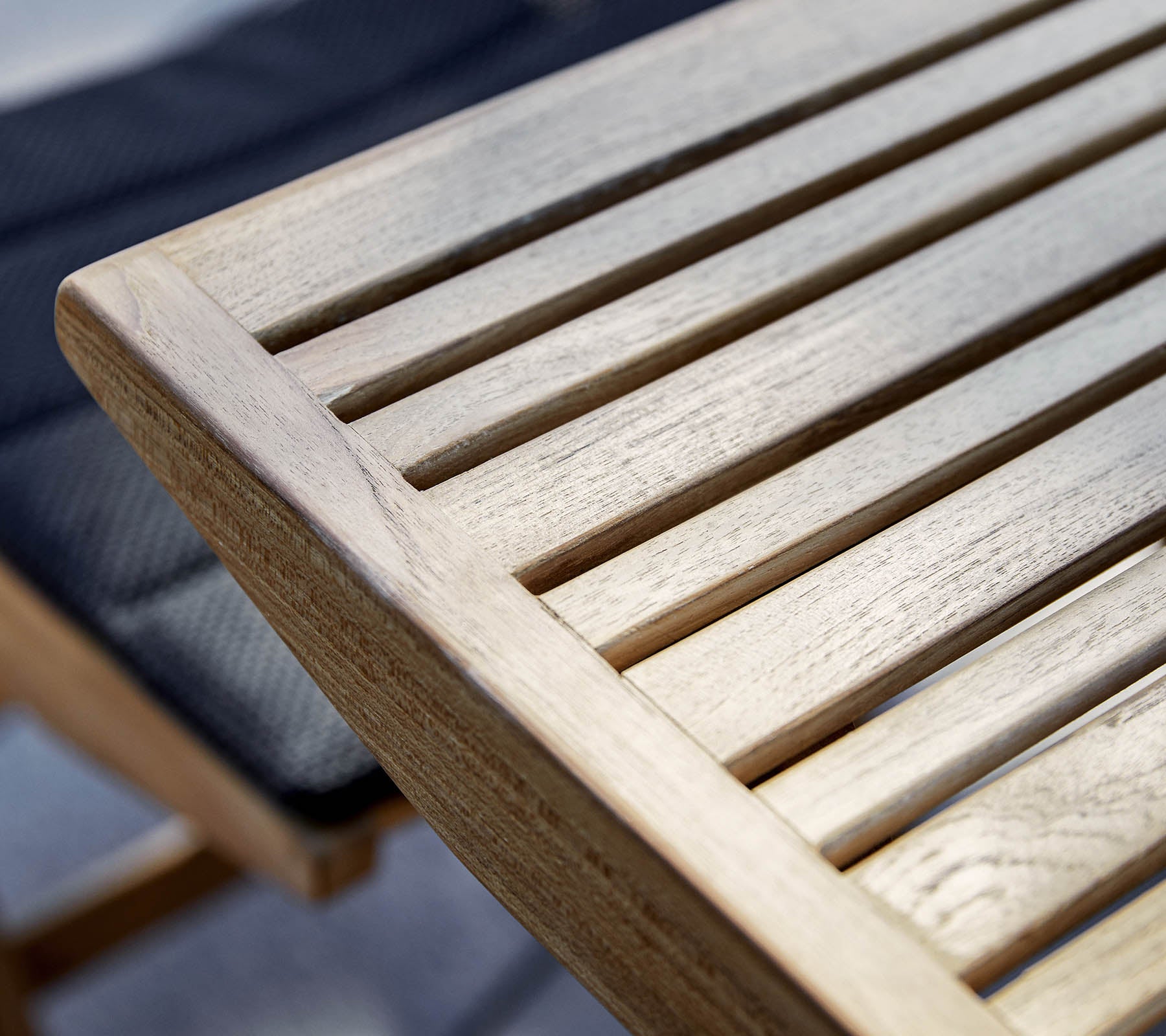 Primer plano del borde de una mesa de madera con diseño de listones, que muestra la veta natural y la textura de la madera.