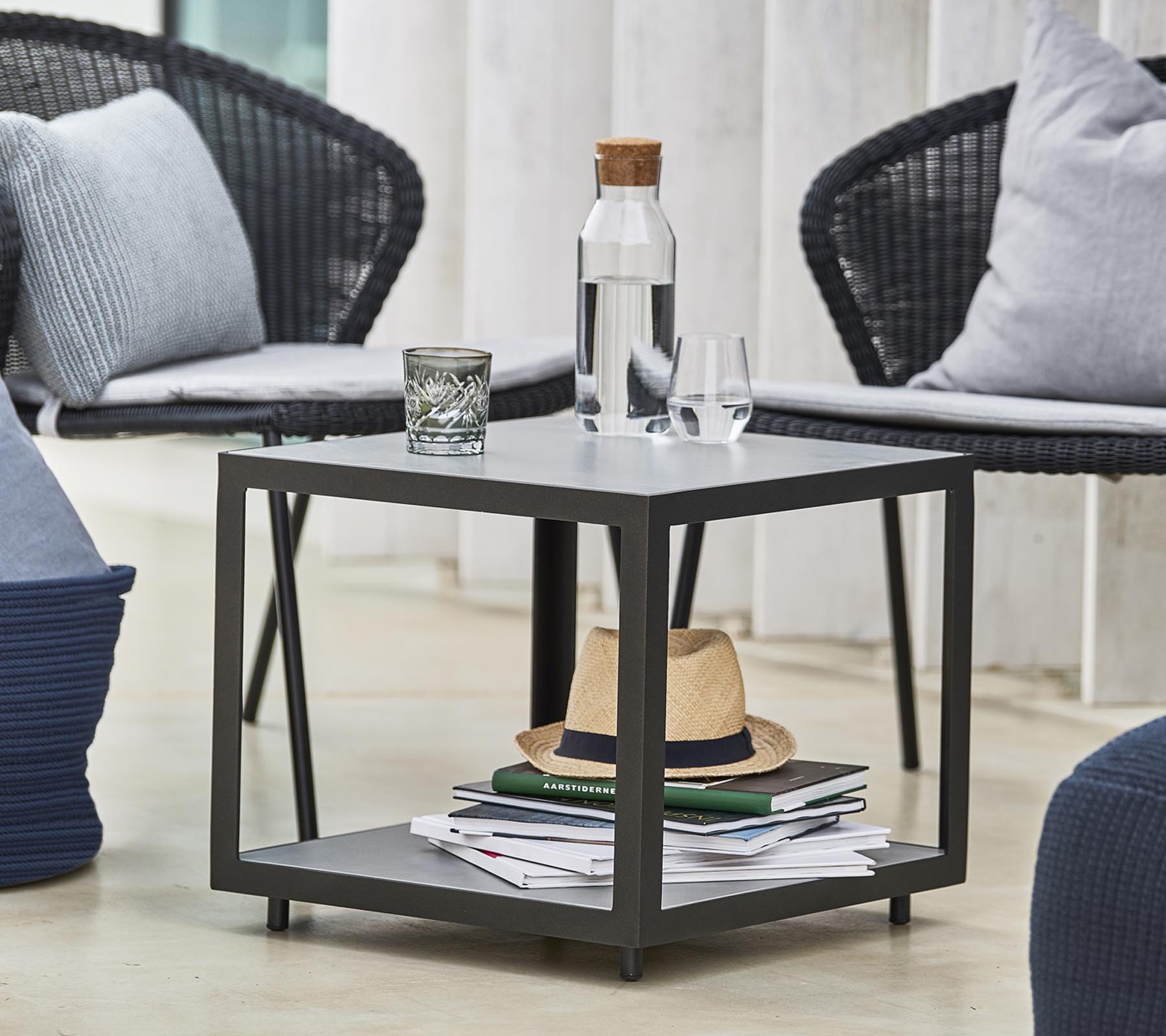 Una mesa moderna con una botella de agua, un vaso y elementos decorativos, rodeada de sillas y cojines elegantes.