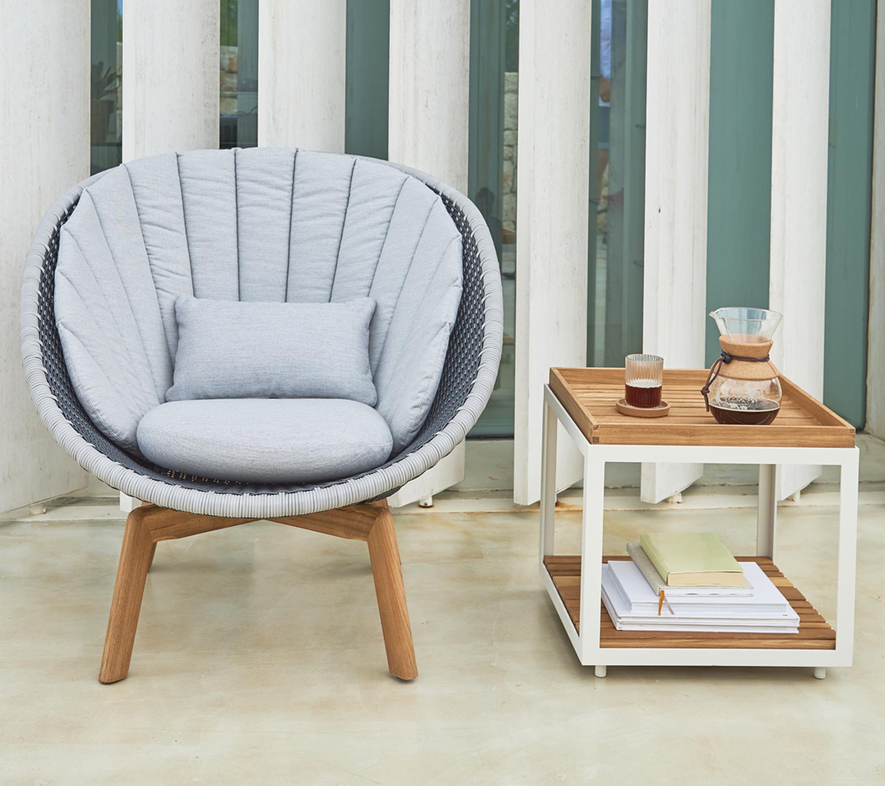 Silla redonda acogedora con cojines suaves junto a una mesa auxiliar ordenada que sostiene bebidas y libros.