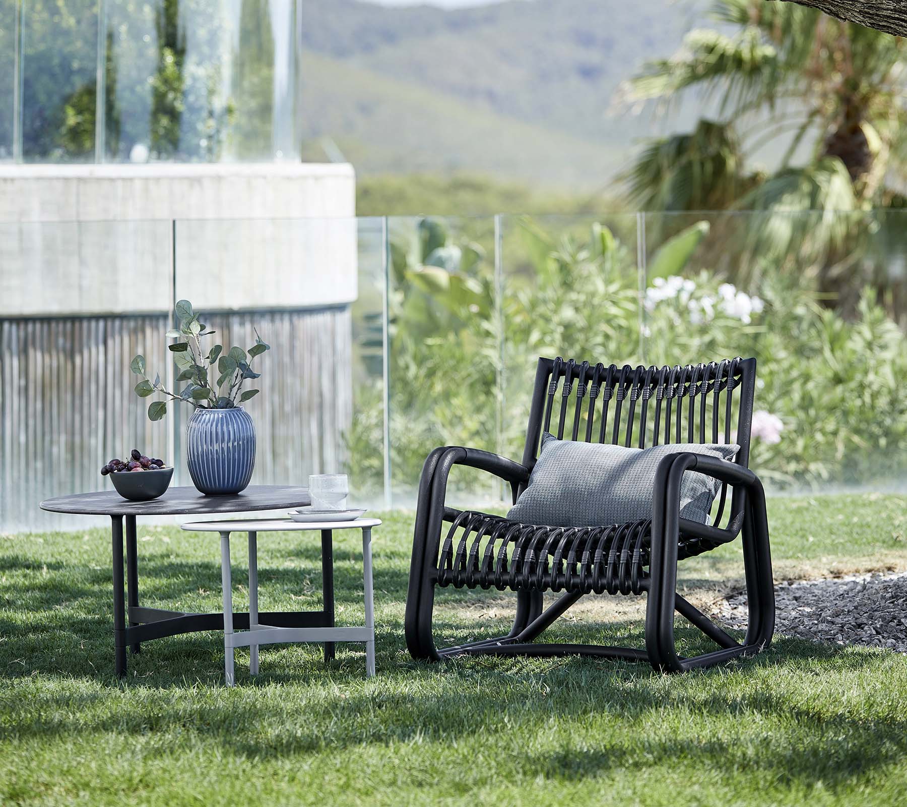 Sillón contemporáneo con un diseño estampado, acompañado de una mesa auxiliar con un jarrón y una planta en maceta, situado en un paisaje natural.