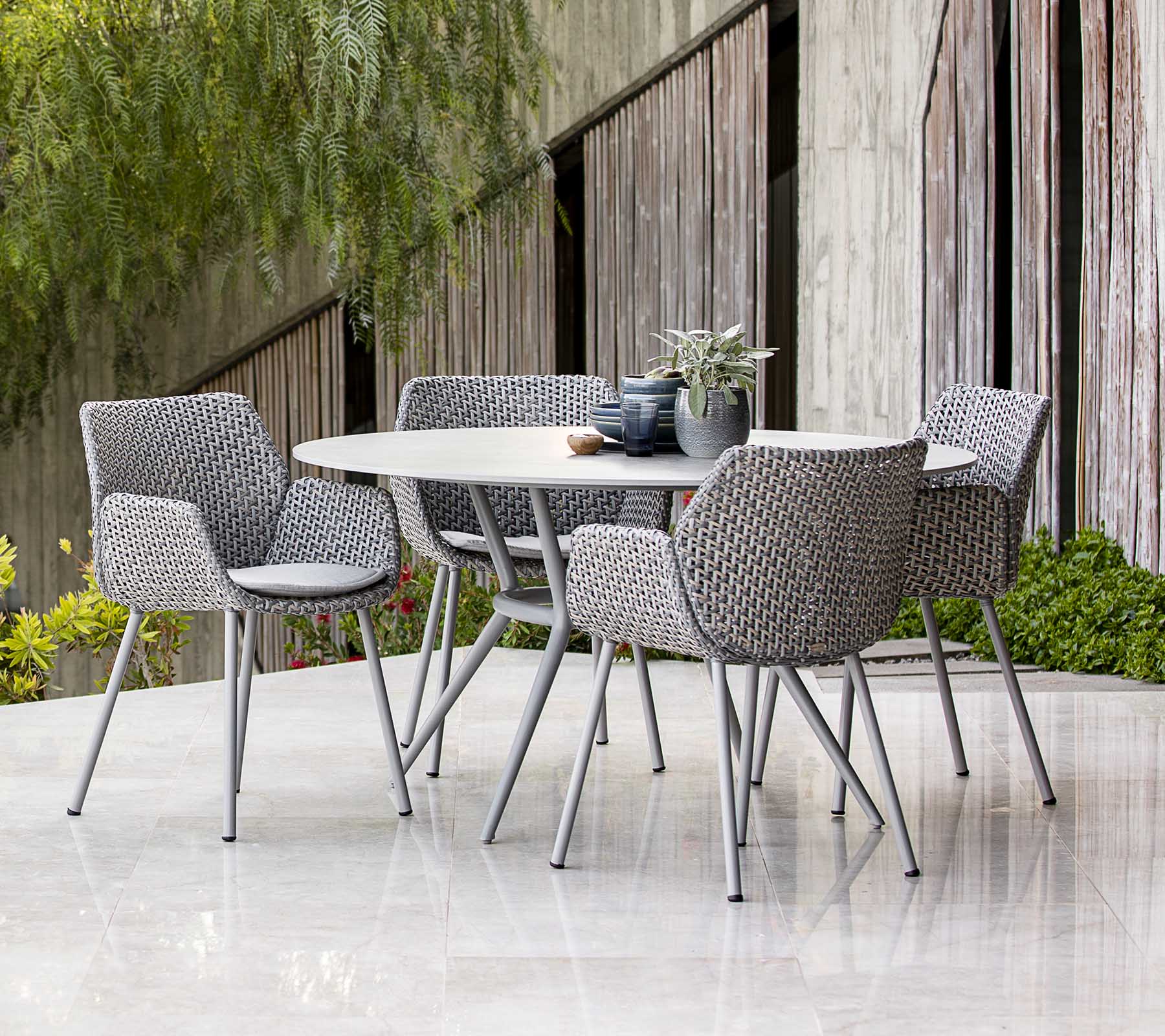 Conjunto de mesa de comedor al aire libre contemporáneo con sillas trenzadas, decorado con plantas y decoración de mesa, con una estética moderna.