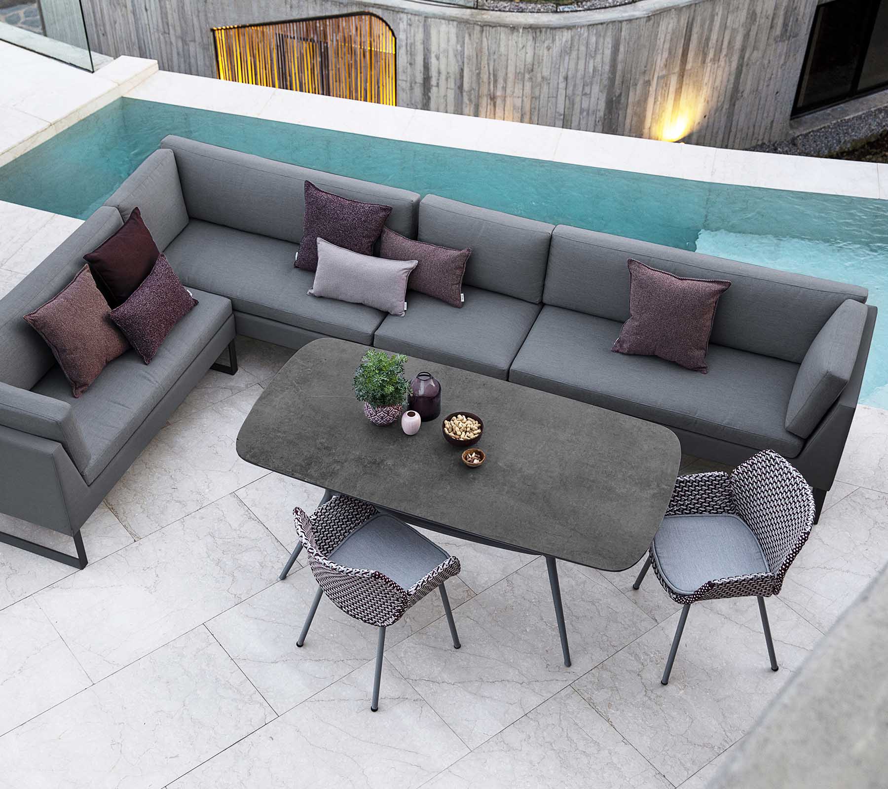 Arreglo de asientos al aire libre moderno con un sofá seccional gris, cojines decorativos y una mesa de comedor elegante rodeada de sillas elegantes.