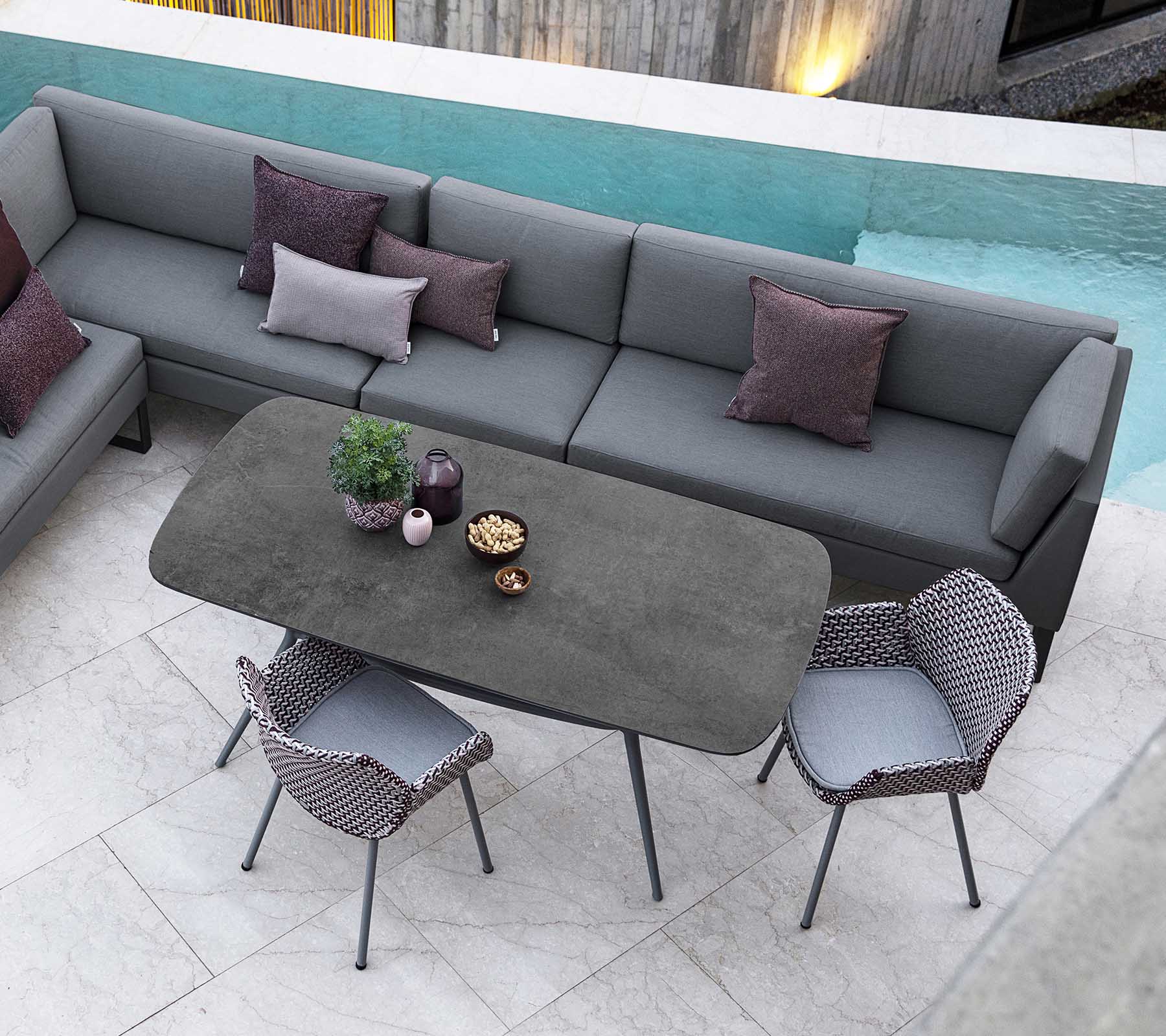 Moderna área de estar al aire libre con un sofá modular con cojines, una mesa rectangular elegante y sillas con estilo, complementadas con vista a la piscina.
