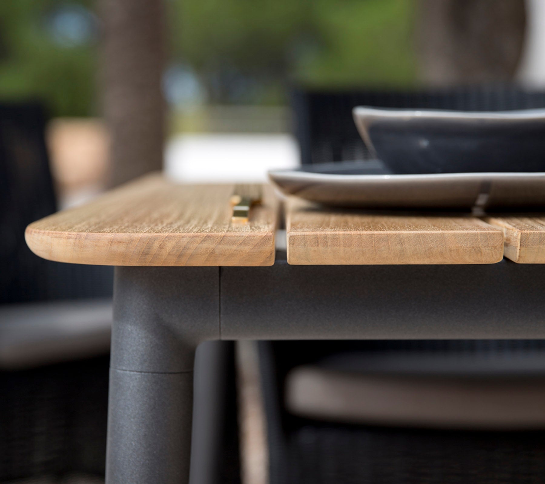 Primer plano de un borde de mesa de madera con un acabado suave, con un plato negro colocado encima, mostrando un diseño moderno.