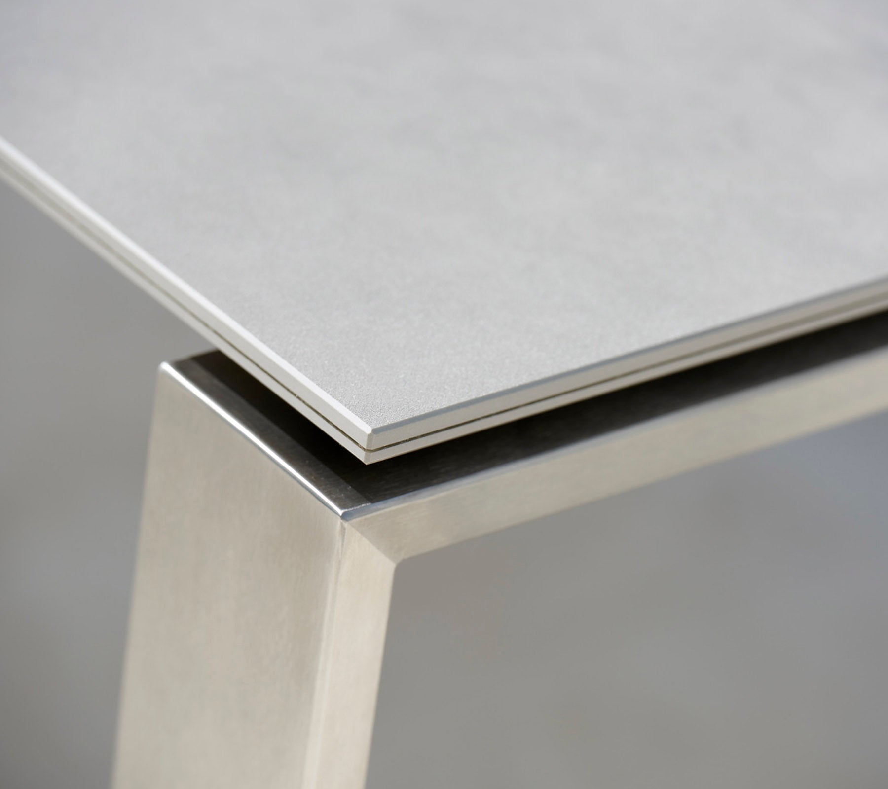 Primer plano de una mesa moderna con una suave parte superior gris y una base de acero inoxidable, destacando los materiales contrastantes y las líneas limpias.