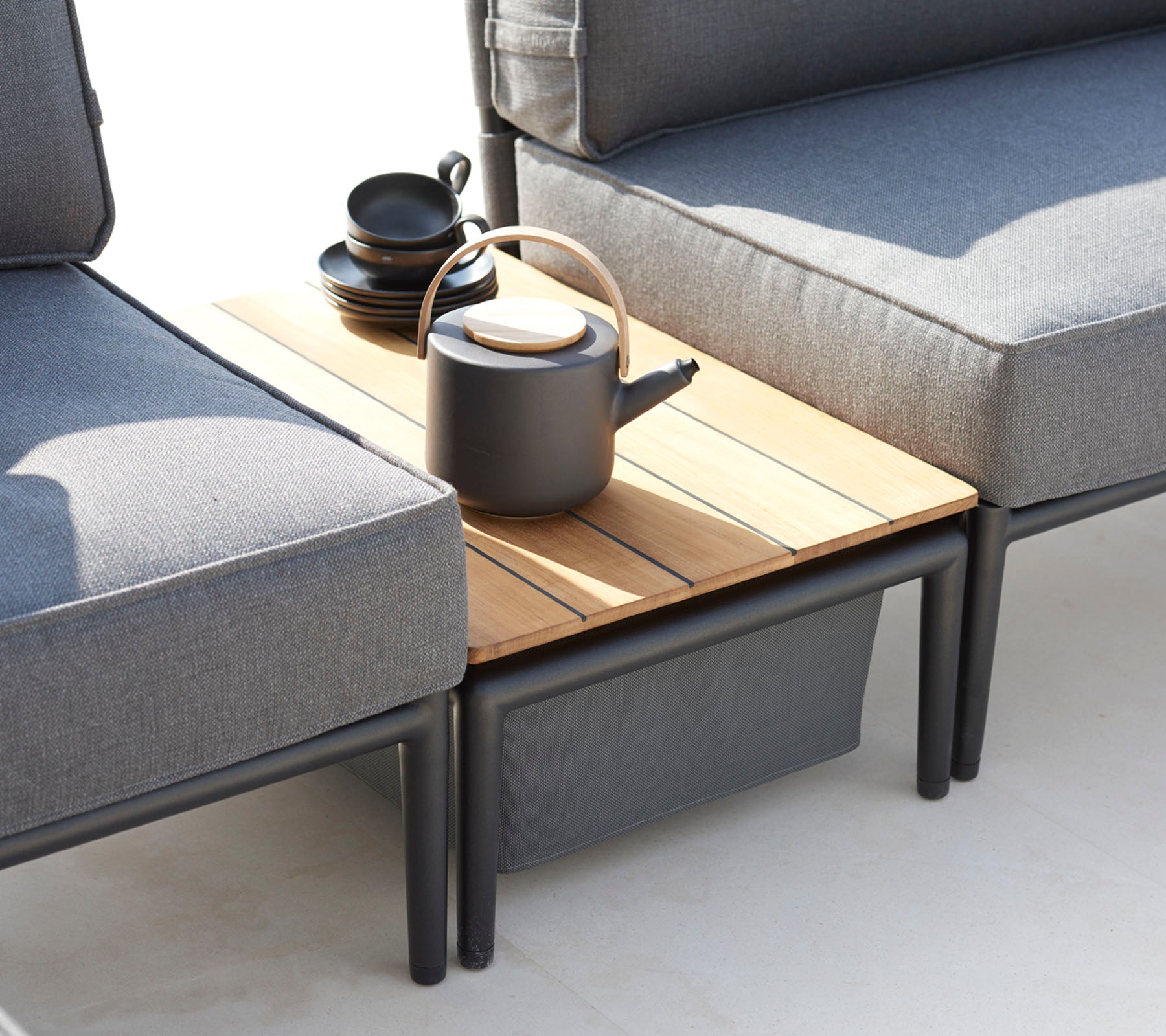 Dos sofás grises flanquean una mesa auxiliar de madera, adornada con una tetera negra y varias tazas, creando un área de asiento acogedora.