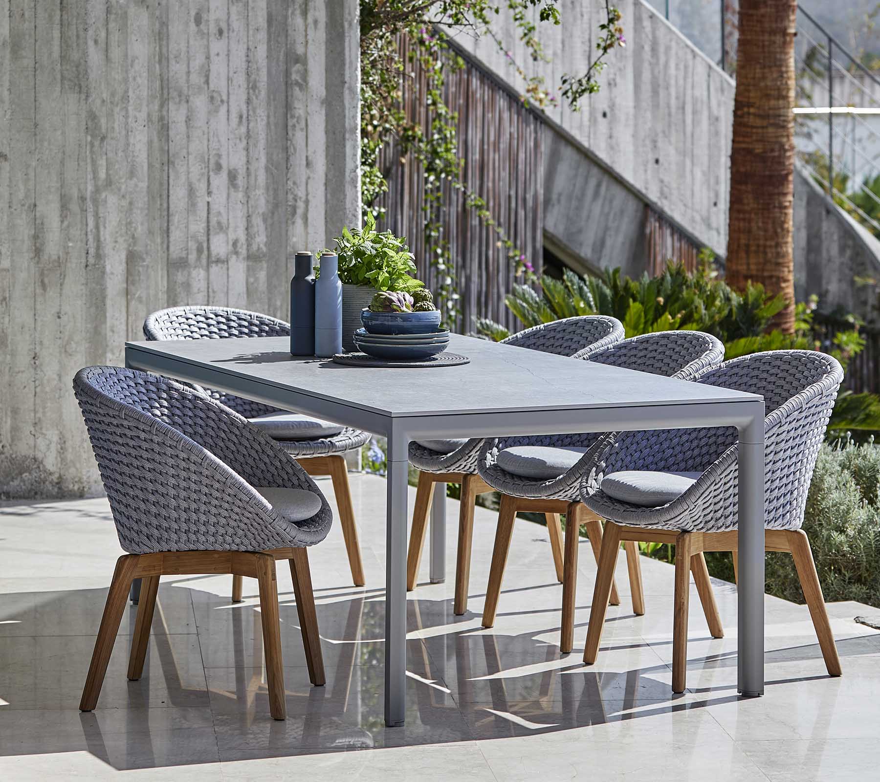 Set de comedor moderno con una mesa gris y sillas tejidas con patas de madera, dispuestas ordenadamente con elementos decorativos sobre la mesa.