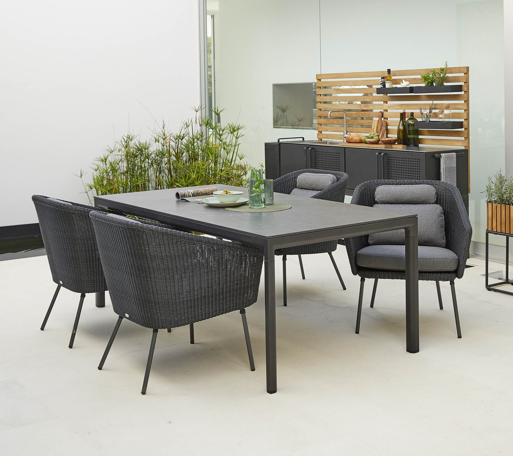 Conjunto moderno de comedor al aire libre con una mesa elegante y cuatro sillas elegantes con cómodos cojines, rodeado de vegetación.