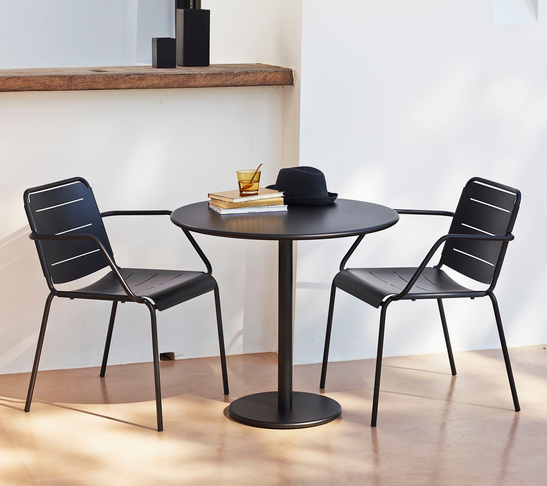 Una mesa redonda con dos sillas negras, adornada con un sombrero y libros, creando un área de descanso elegante y acogedora.