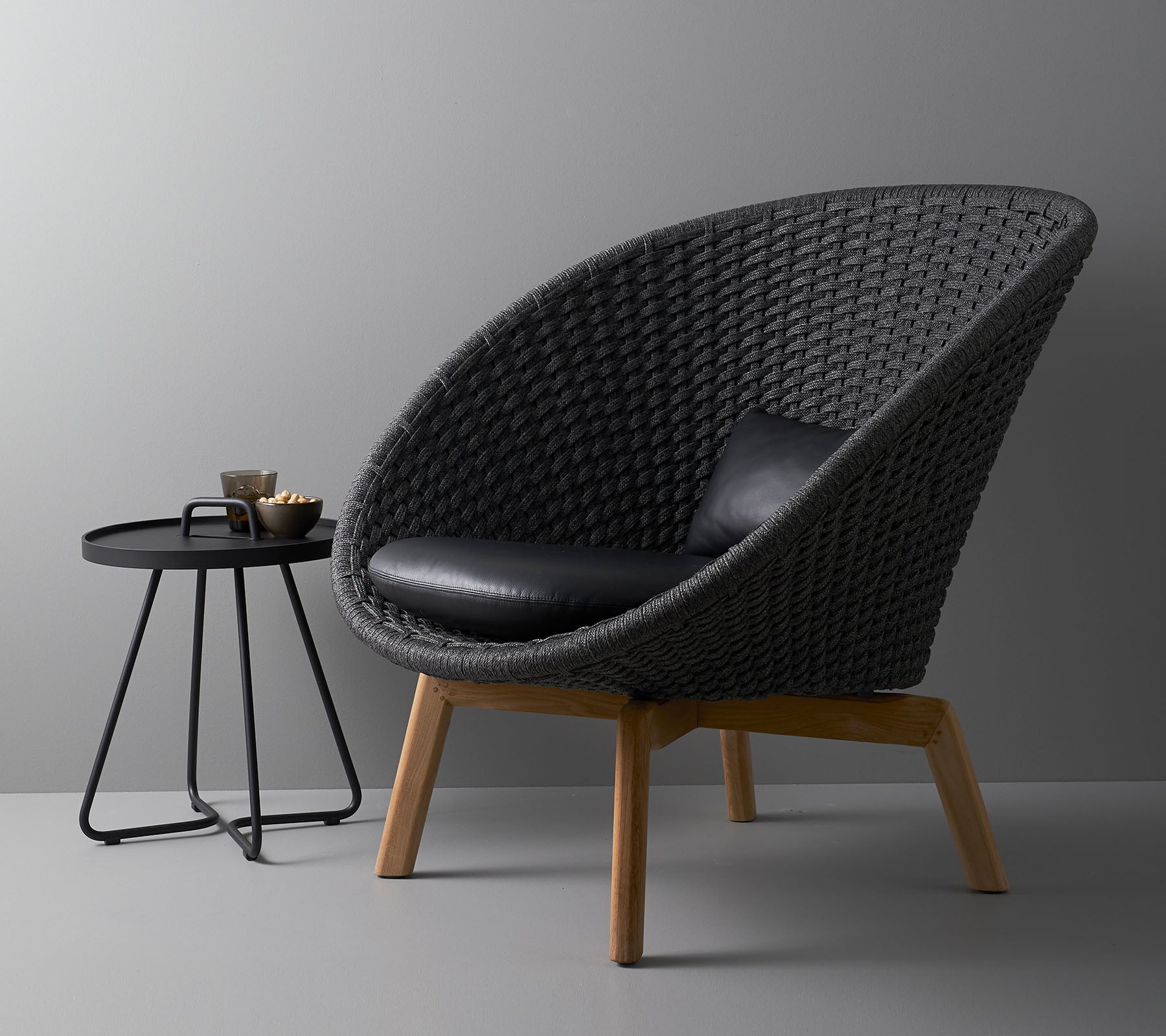Silla tejida con estilo con un cojín negro y una mesa auxiliar redonda moderna, ideal para espacios de vida contemporáneos.