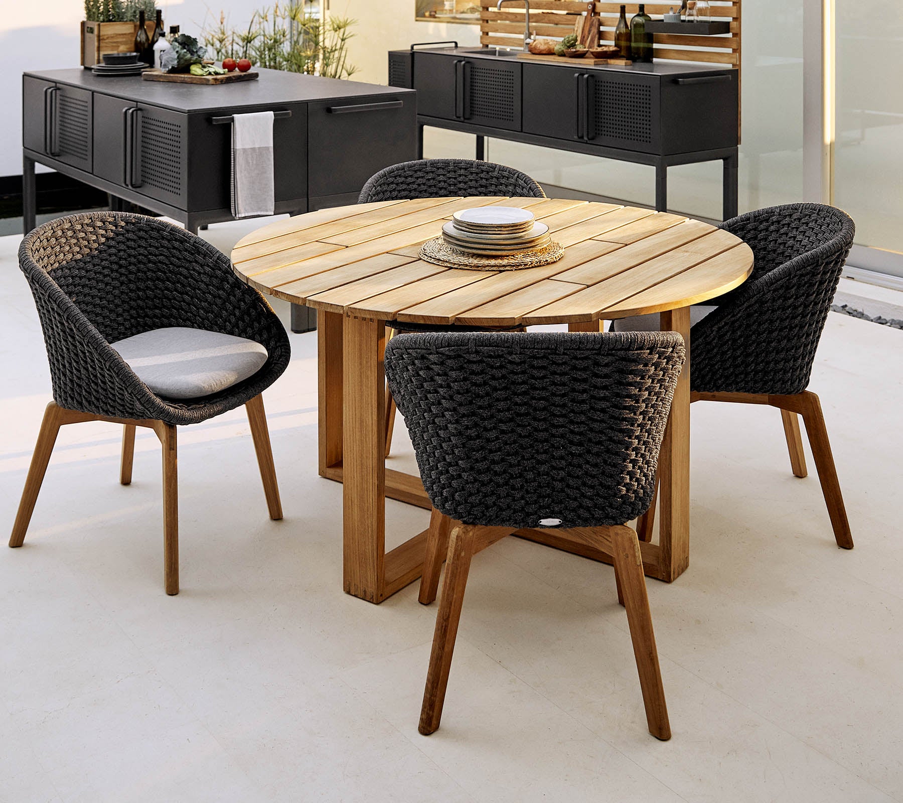 Mesa redonda de madera con cuatro elegantes sillas trenzadas, perfecta para cenas y reuniones sociales. Disposición de asientos al aire libre elegante y acogedora.