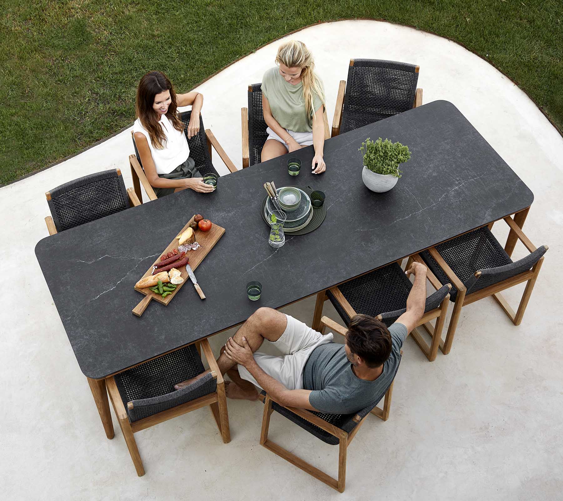 Un grupo de personas disfrutando de una comida alrededor de una mesa grande, con platos, bebidas y un centro de planta. Ambiente de comedor informal.