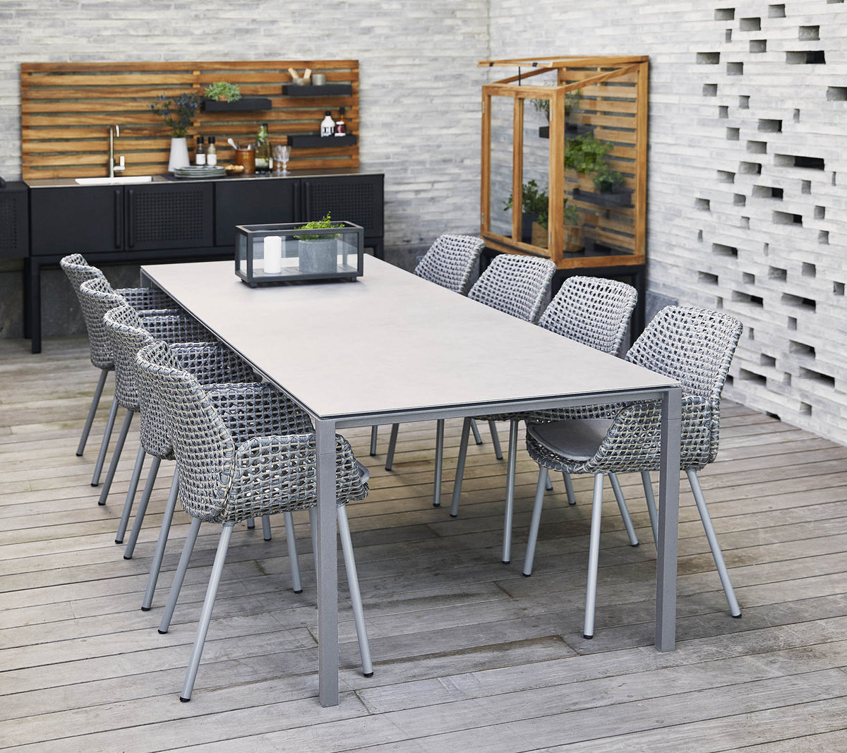 Una mesa larga y elegante rodeada de sillas tejidas, con un centro de mesa y elementos decorativos en un entorno contemporáneo.