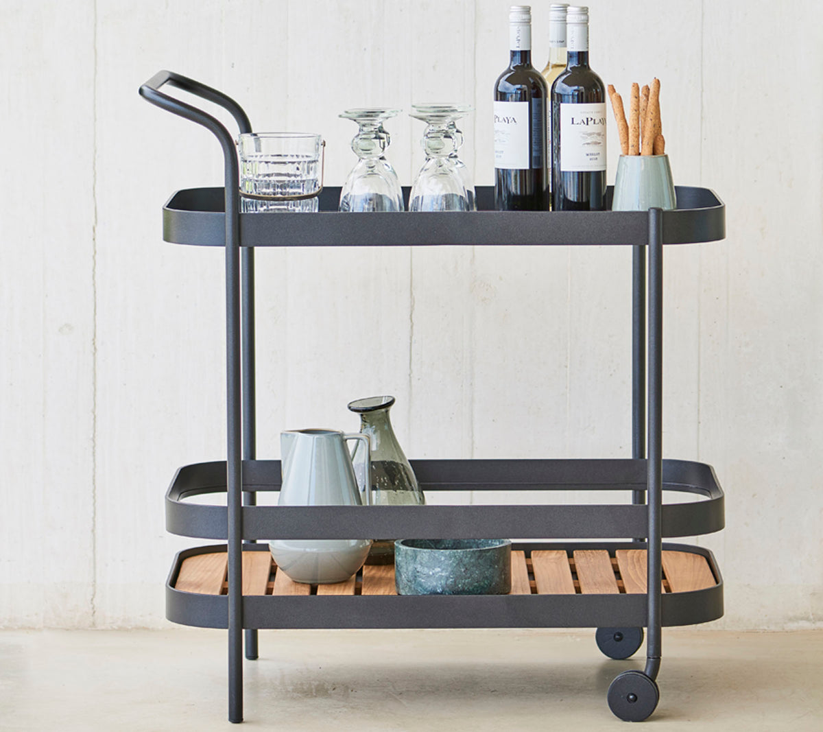 Un carrito de bebidas elegante con cristalería, botellas de vino y utensilios en tres niveles, con un marco de metal elegante y detalles de madera.
