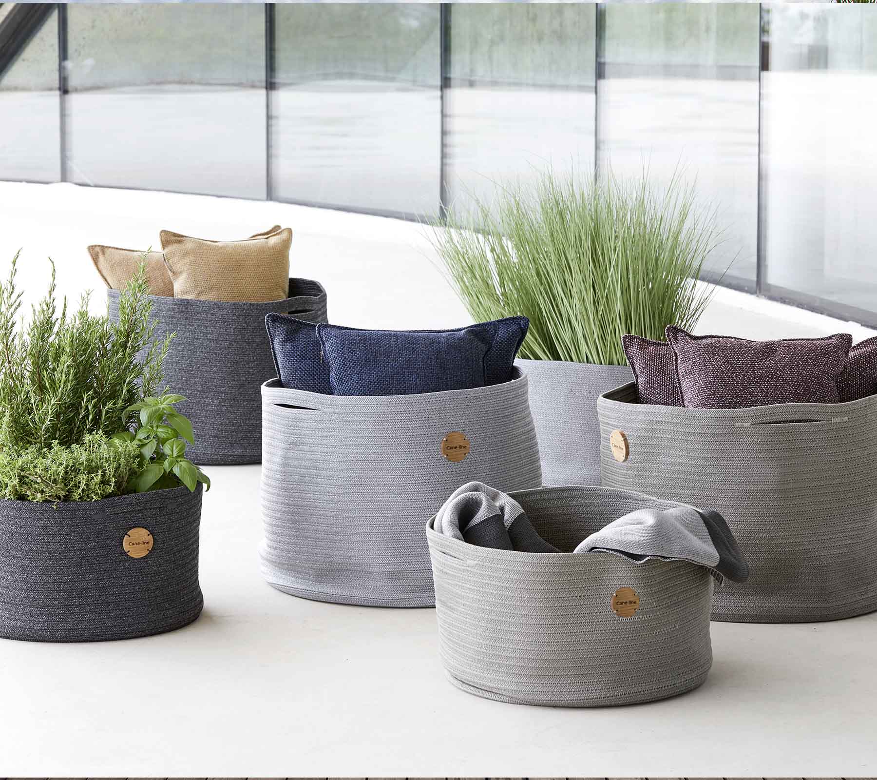 Una variedad de cestos de almacenamiento tejidos y elegantes en diferentes tamaños, con cojines vibrantes y vegetación para un toque decorativo.