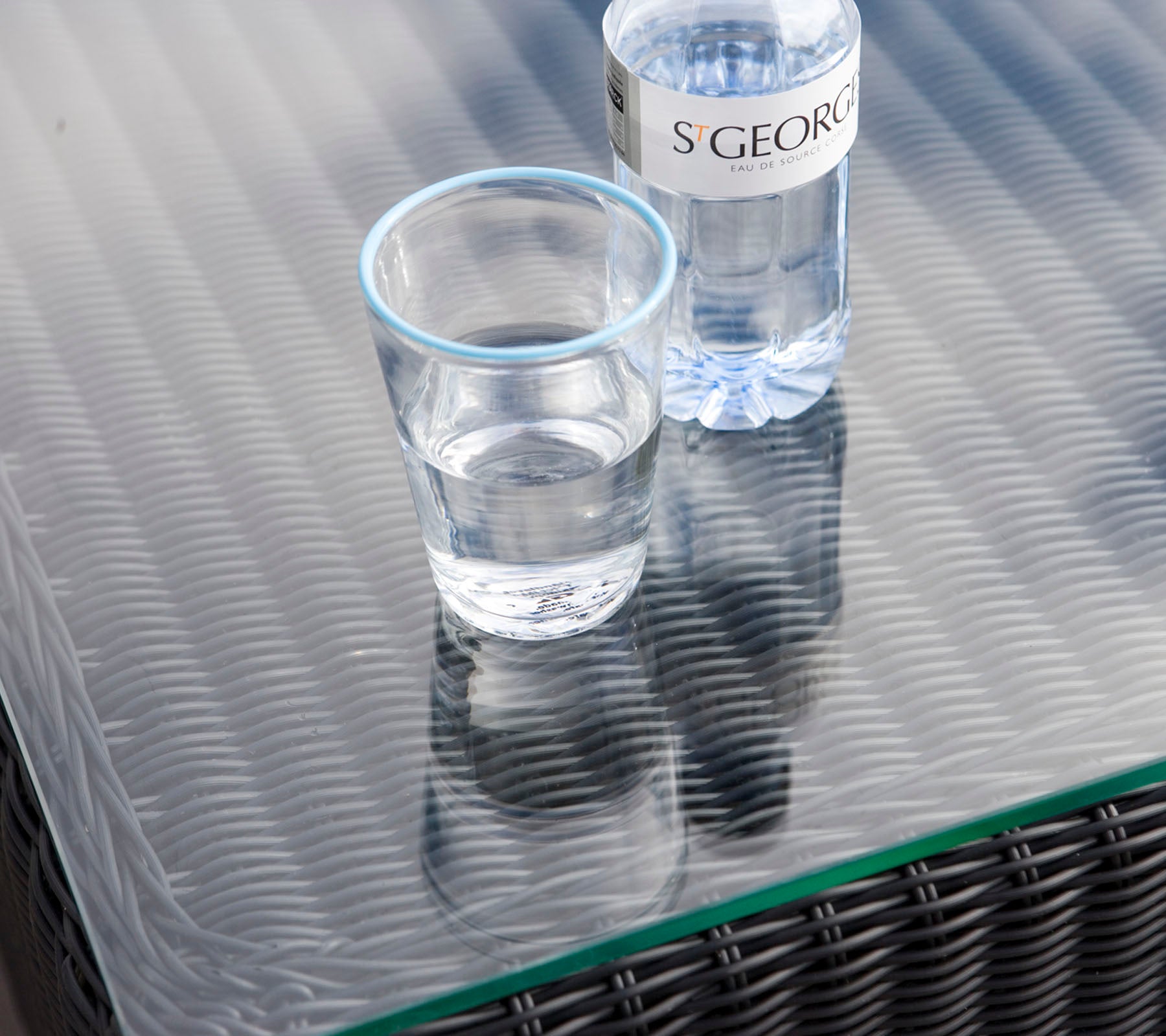 Un vaso claro con agua al lado de una botella de agua sobre una superficie de mesa texturizada.