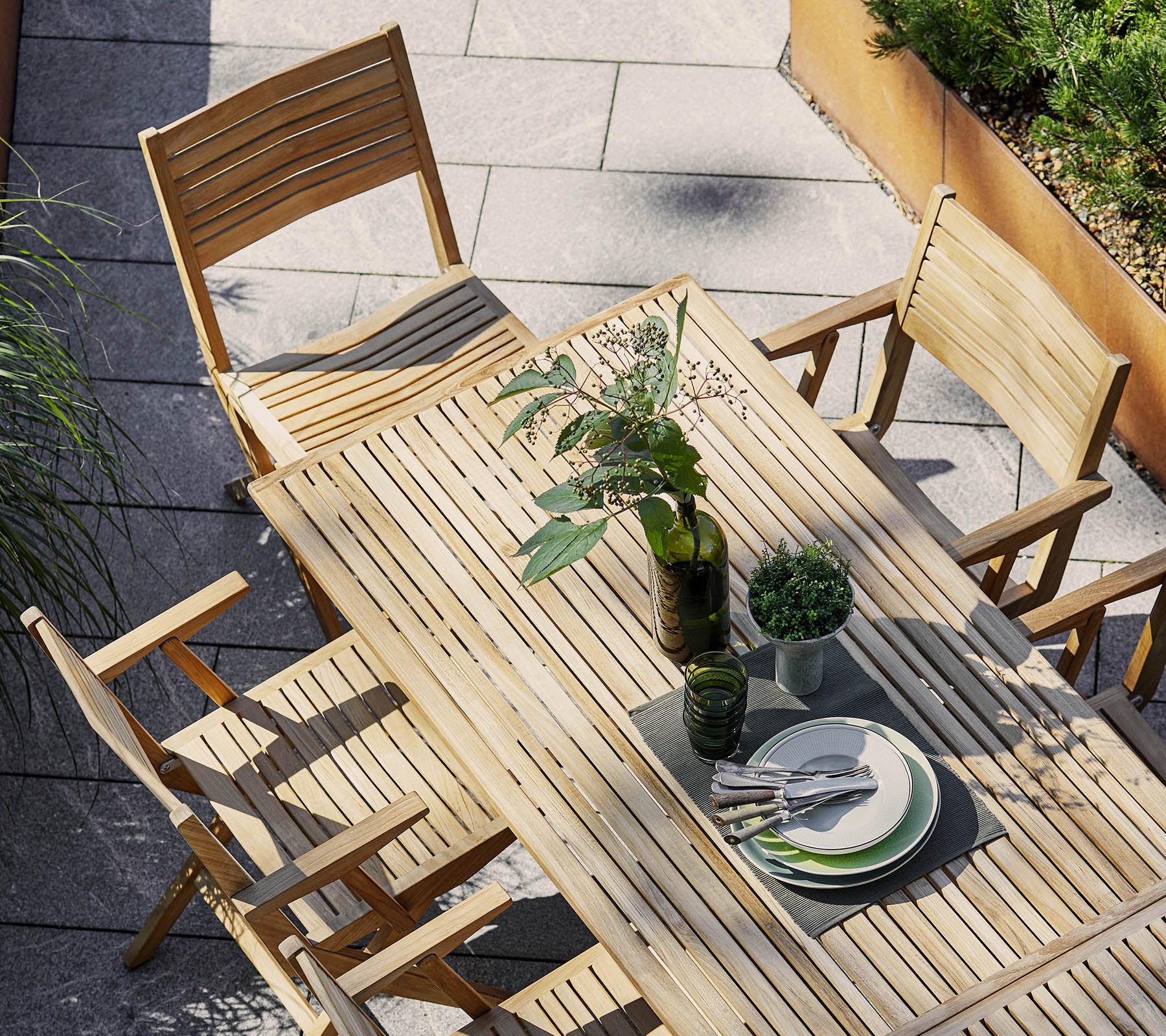 Conjunto de comedor de madera con una mesa rectangular y sillas plegables, adornado con vegetación y vajilla para un ambiente acogedor.
