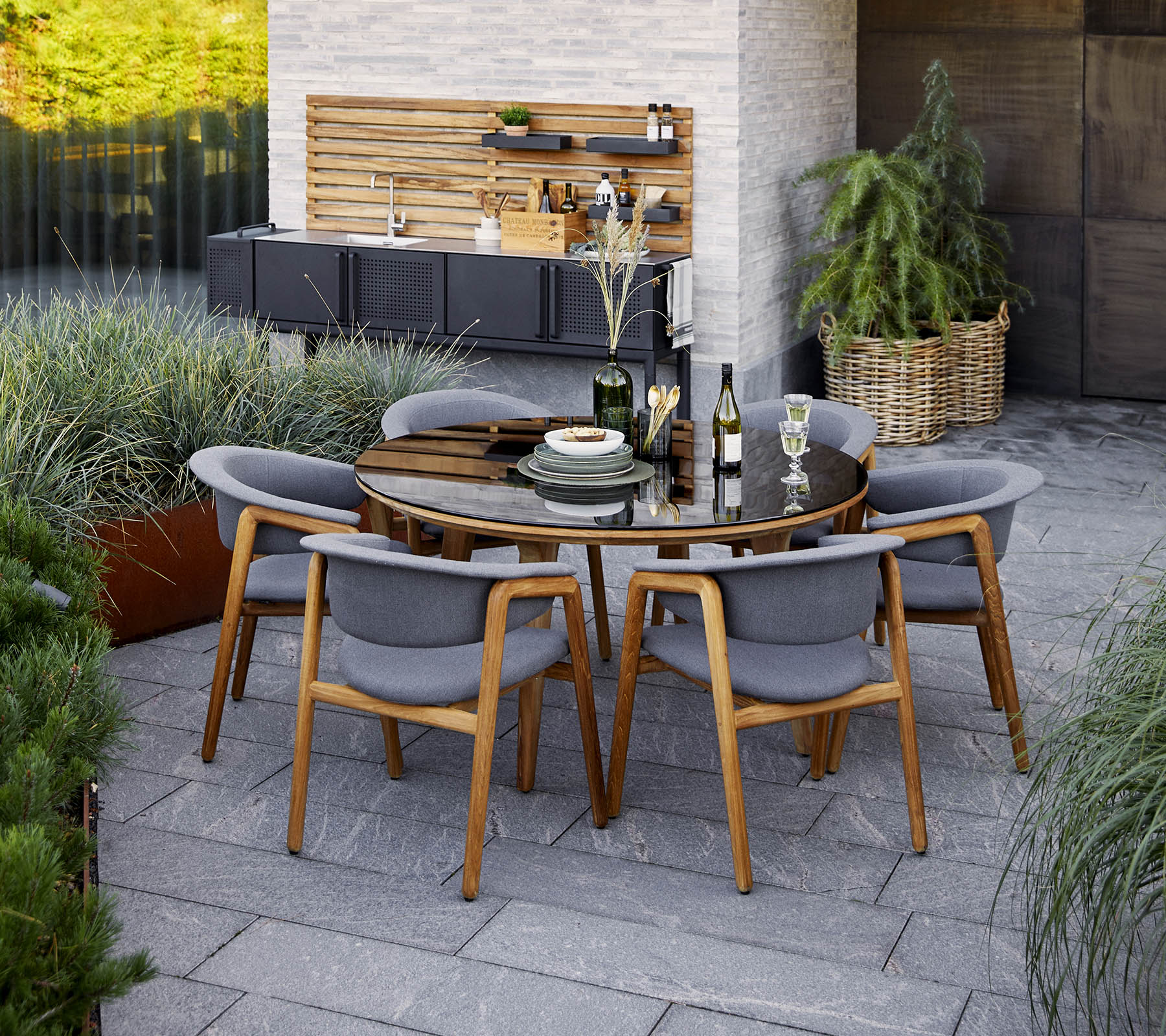 Un conjunto de mesa de comedor redonda moderna con sillas grises, que presenta elementos decorativos y vegetación al fondo.