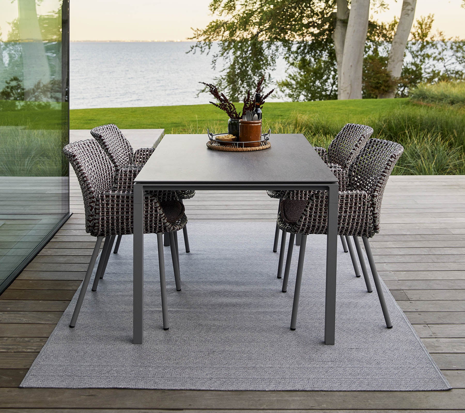 Una mesa de comedor moderna con cuatro sillas tejidas elegantes, adornada con un centro de mesa decorativo de planta sobre una alfombra suave.