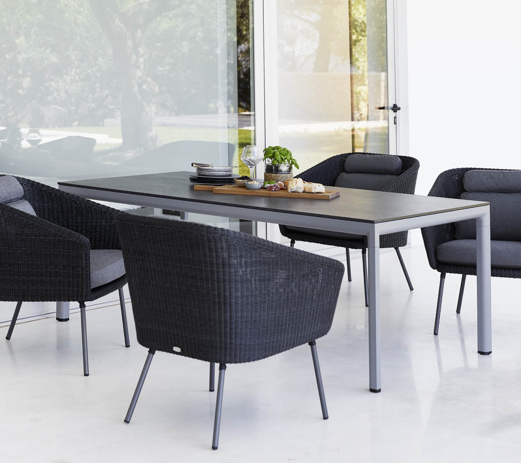 Una mesa de comedor moderna rodeada de cuatro sillas de exterior negras y elegantes, con un centro de mesa y vegetación sobre la mesa.