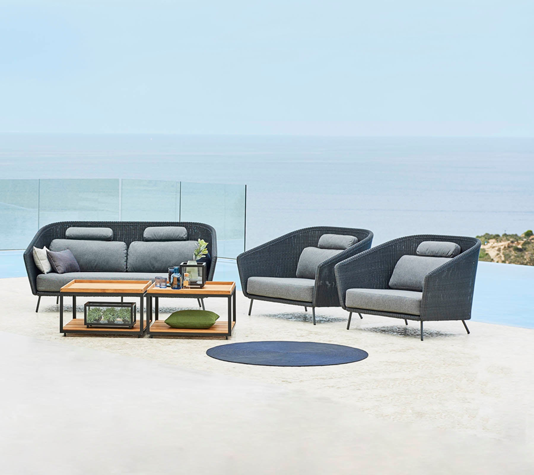 Arreglo de asientos al aire libre elegante con un sofá y dos sillas, complementado con una mesa de café y elementos decorativos, con un fondo pintoresco.