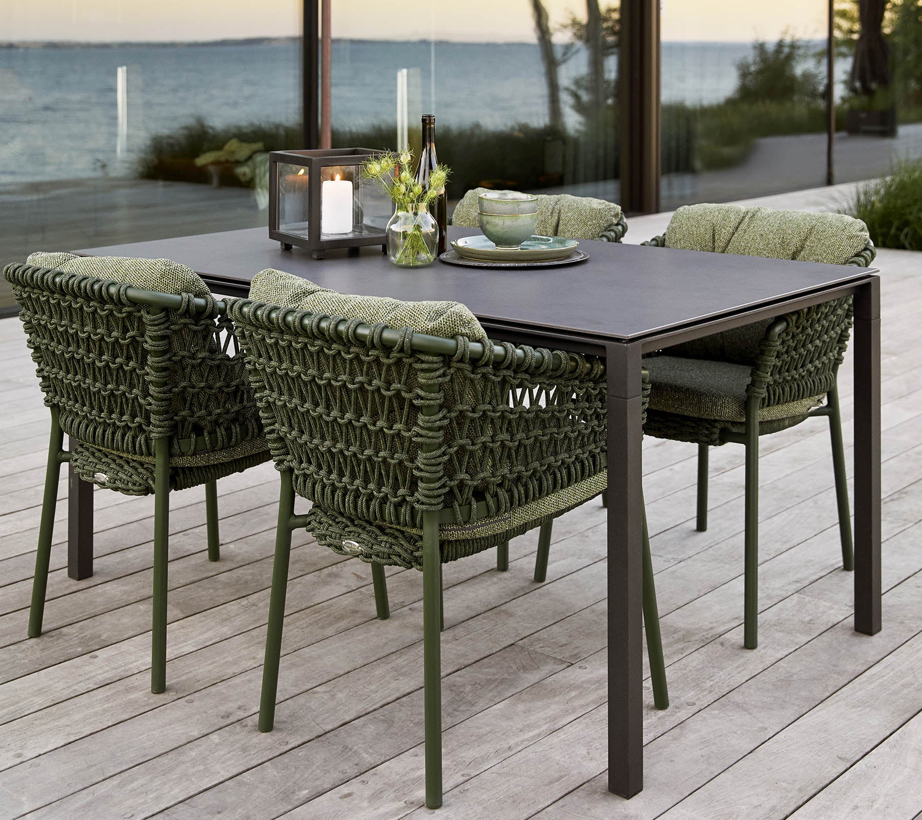 Conjunto de comedor al aire libre elegante que incluye una mesa rectangular y cuatro sillas tejidas con cojines, complementado con un centro de flores.