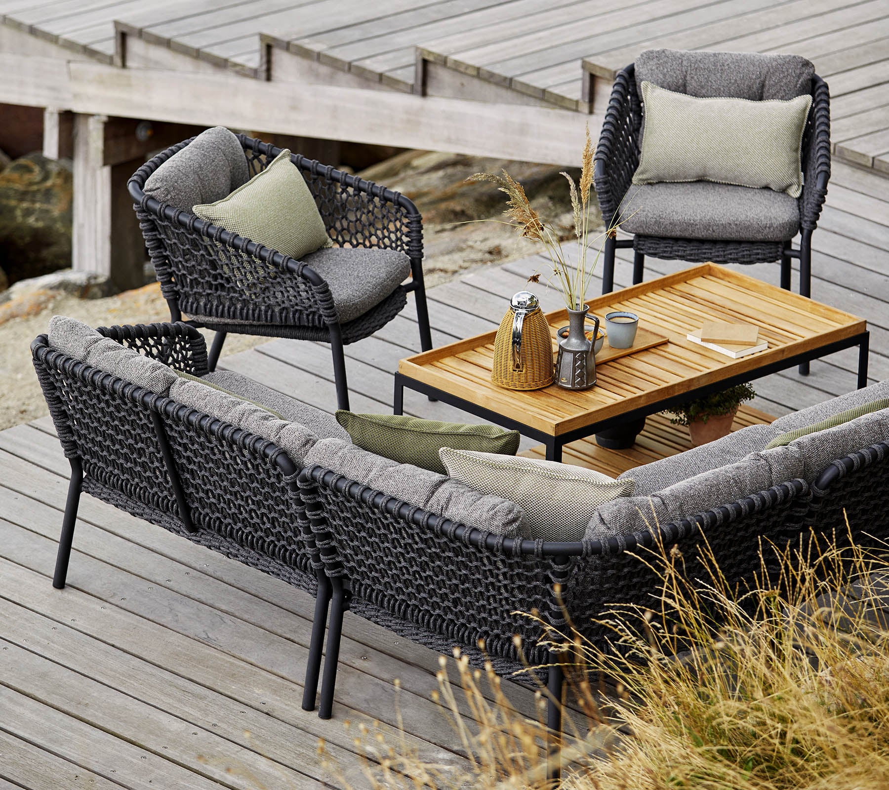 Conjunto de asientos al aire libre elegante que cuenta con un sofá acogedor, dos sillas y una mesa de café de madera, acentuado con cojines suaves y elementos decorativos.