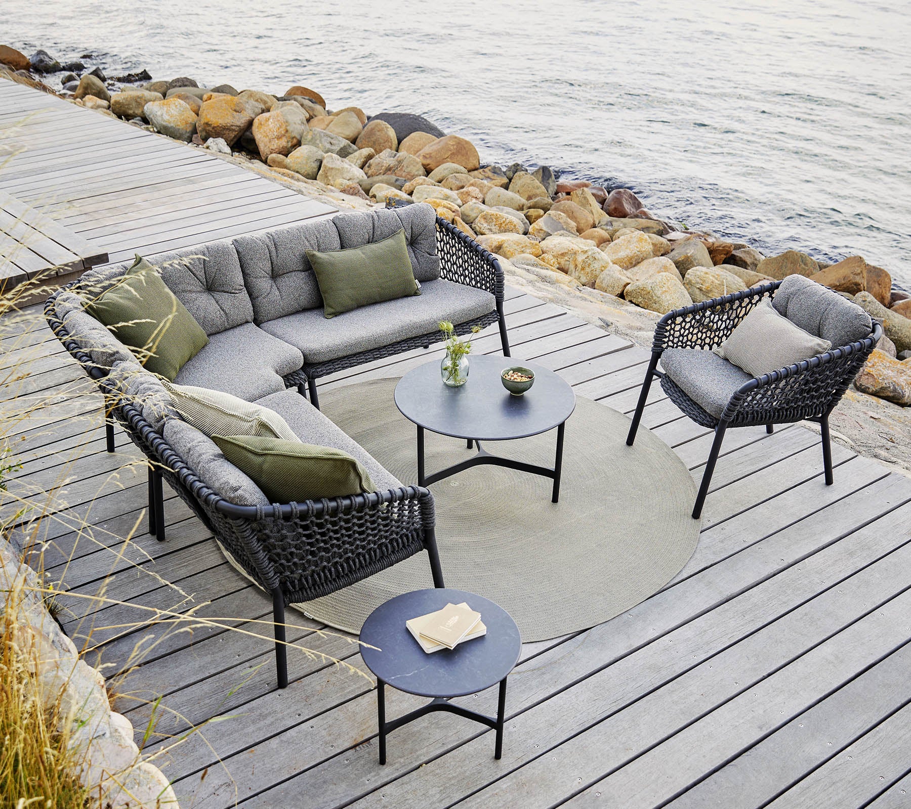 Una elegante disposición de asientos al aire libre que incluye un sofá modular y sillas con cojines grises, una mesa redonda y acentos decorativos.