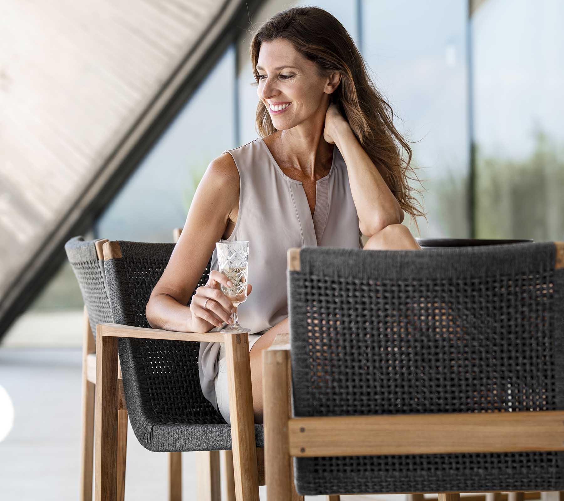 Mujer sonriente sosteniendo una bebida mientras está sentada en una silla elegante, emanando una vibra relajada y elegante. Atmosfera brillante y aireada.