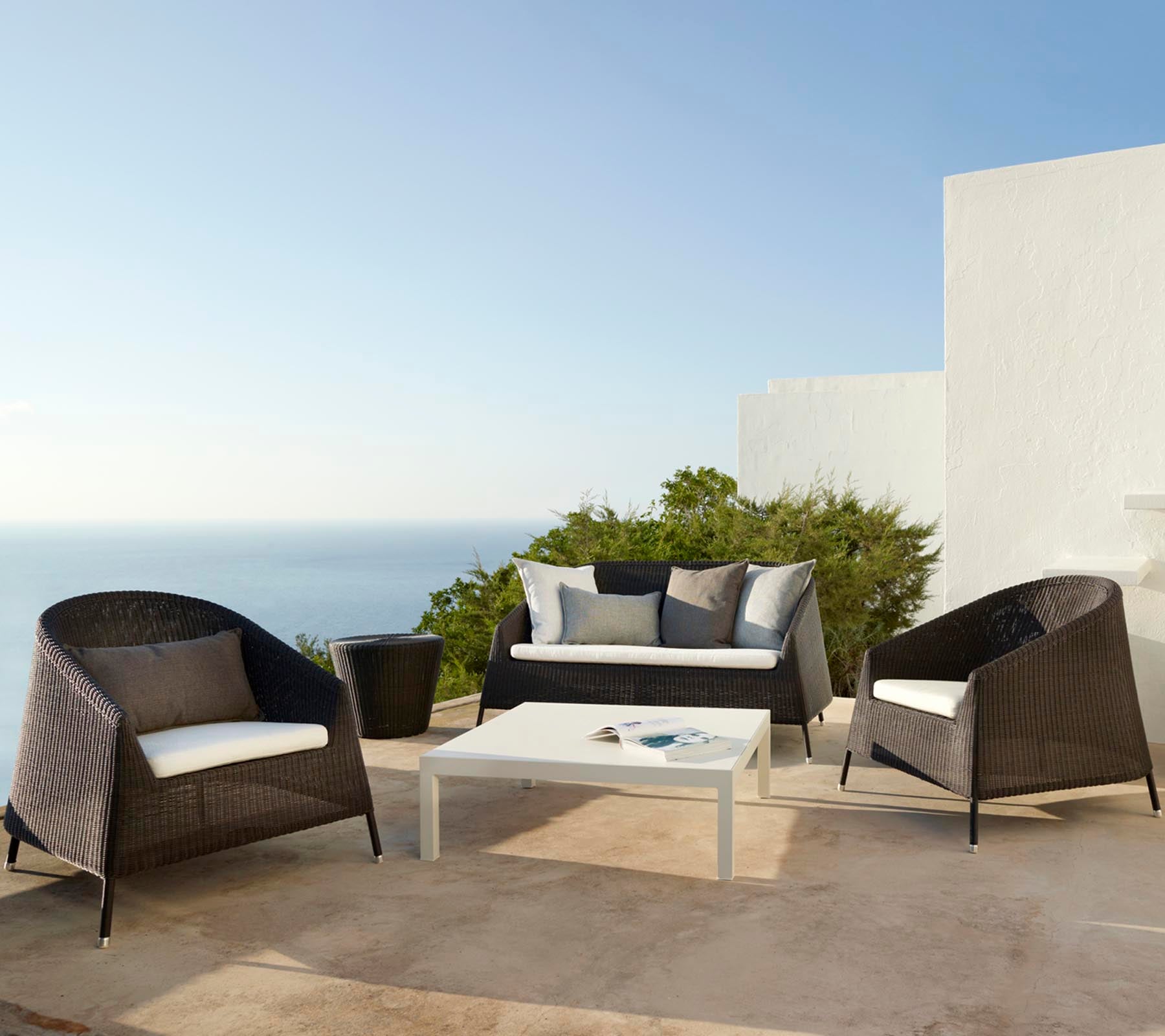 Elegante disposición de asientos al aire libre con un sofá y sillas con cojines, complementada por una mesa con superficie de cristal, ideal para relajarse.