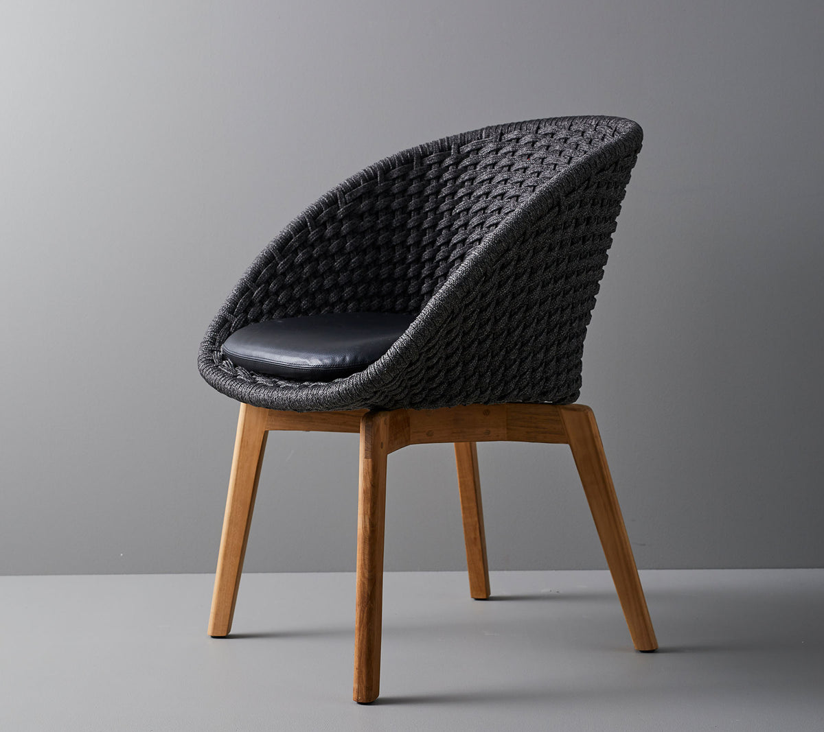 Silla tejida elegante con un cojín cómodo, con patas de madera suaves y cónicas y un diseño moderno adecuado para diversos entornos.