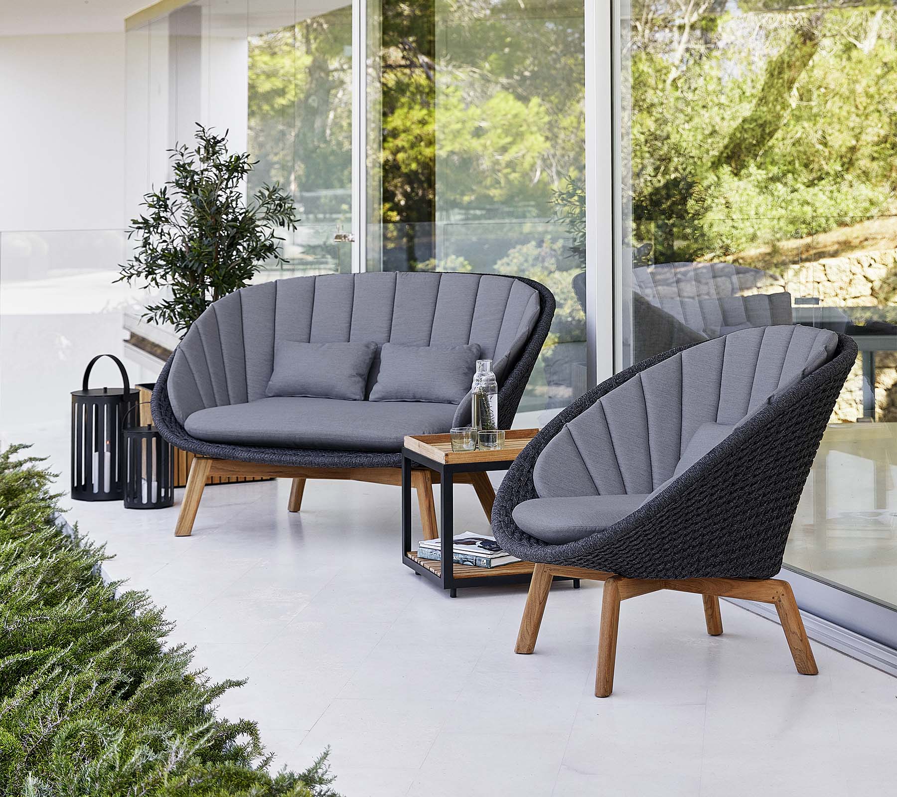 Asientos exteriores elegantes con dos sillas acolchadas y un loveseat, acompañados de una mesa pequeña y una linterna decorativa.
