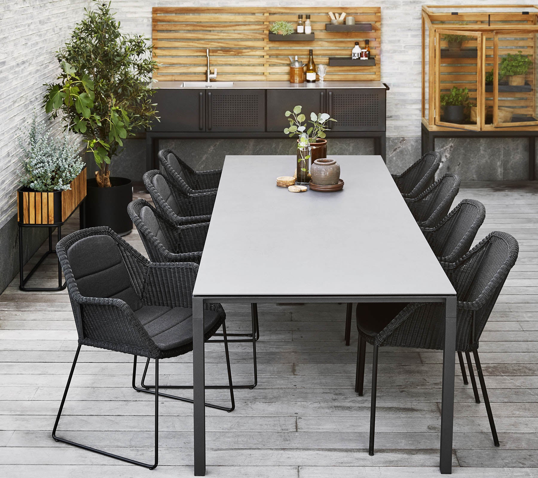 Una configuración de comedor moderna con una mesa larga rodeada de elegantes sillas negras, complementada con plantas decorativas y un fondo de madera.