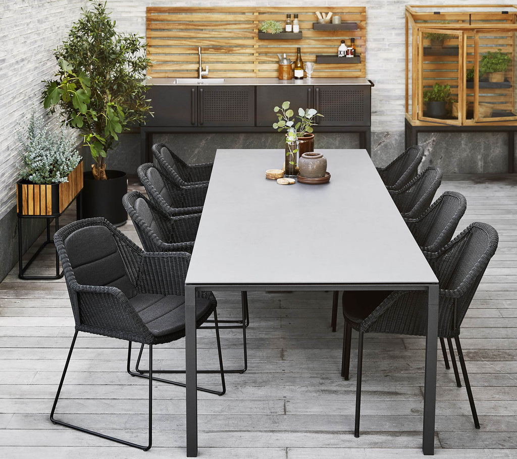 Una configuración de comedor moderna con una mesa larga rodeada de elegantes sillas negras, complementada con plantas decorativas y un fondo de madera.