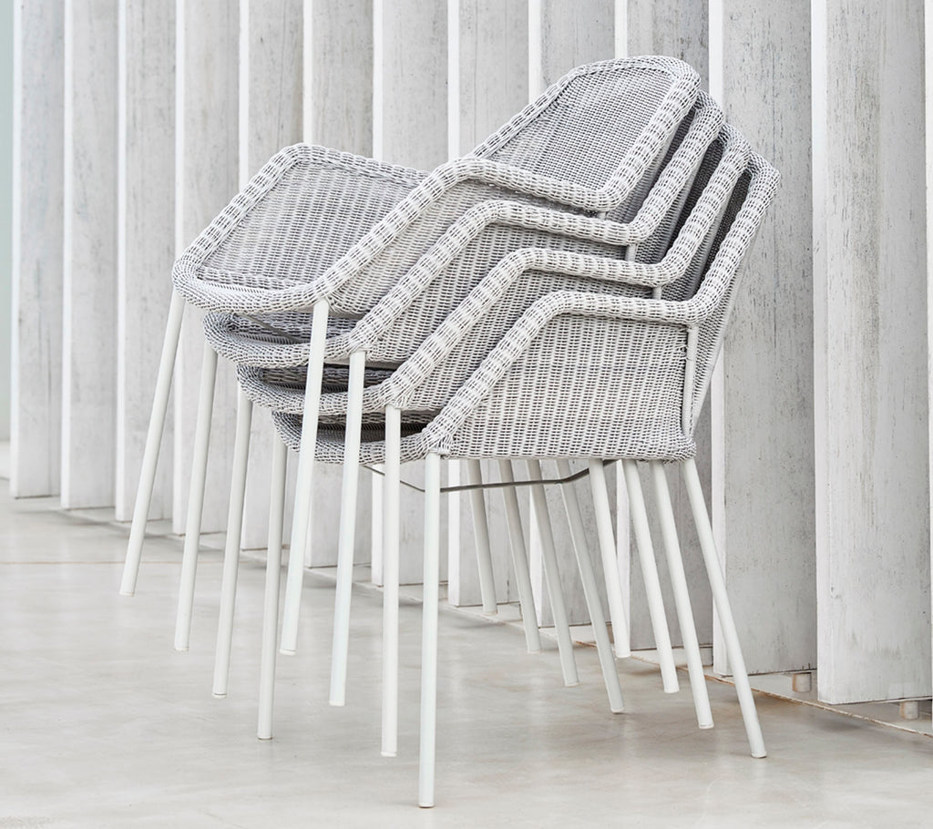 Sillas modernas apiladas con un diseño tejido en gris y blanco, apoyadas contra superficies verticales, mostrando una estética elegante y minimalista.