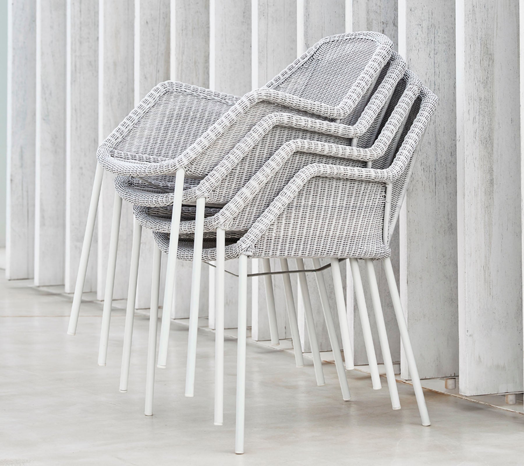 Sillas modernas apiladas con un diseño tejido en gris y blanco, apoyadas contra superficies verticales, mostrando una estética elegante y minimalista.
