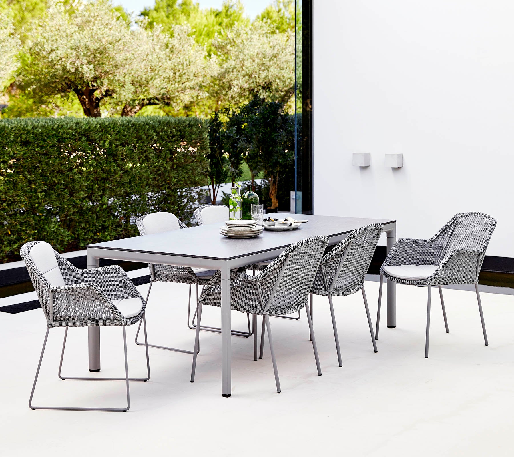 Un conjunto de comedor moderno que presenta una mesa rectangular y seis sillas trenzadas elegantes, rodeadas de vegetación.