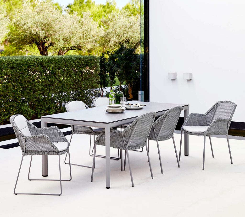 Un conjunto de comedor moderno que presenta una mesa rectangular y seis sillas trenzadas elegantes, rodeadas de vegetación.