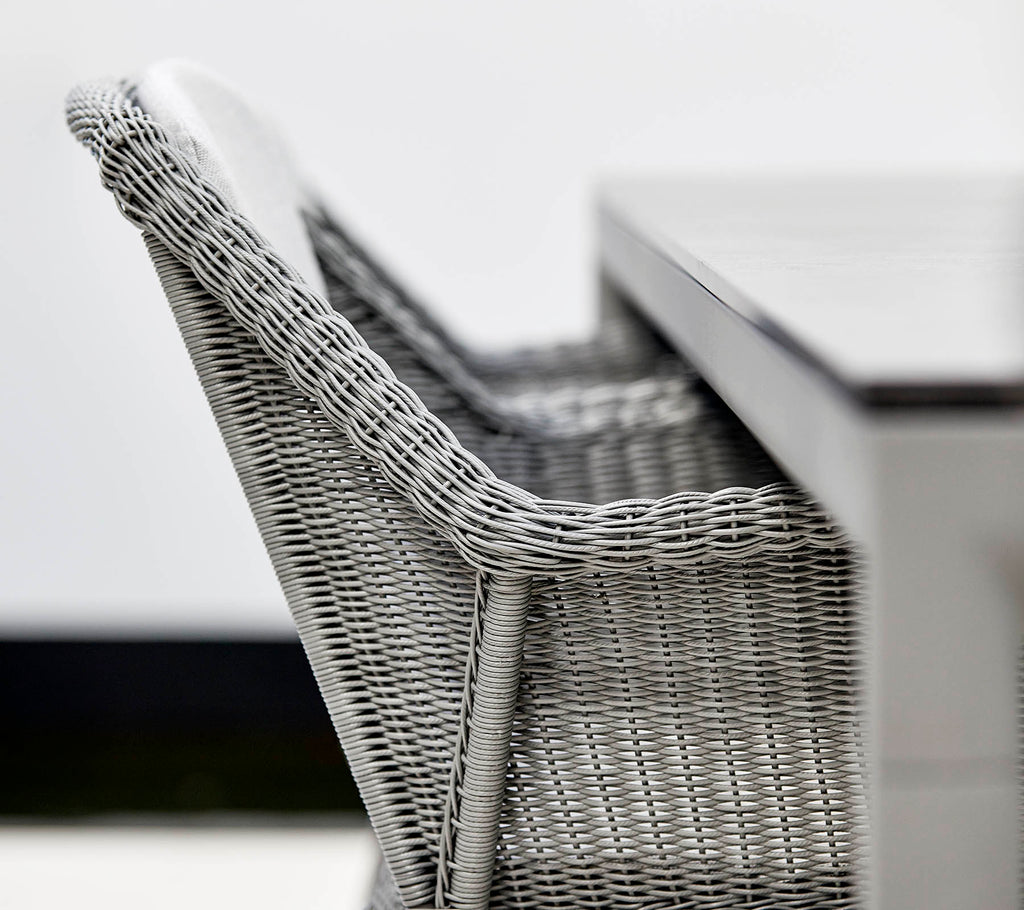 Un primer plano de una silla de mimbre gris elegante junto a una mesa elegante, mostrando un diseño moderno y texturas.