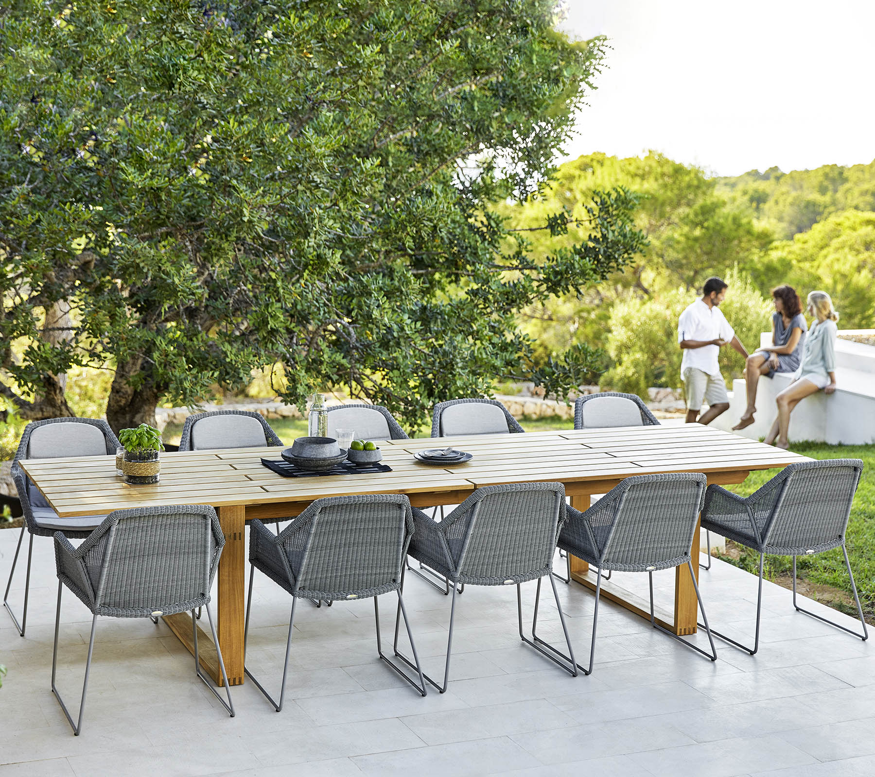 Una espaciosa mesa de comedor con modernas sillas grises, preparada para una comida, rodeada de vegetación y un ambiente relajante.
