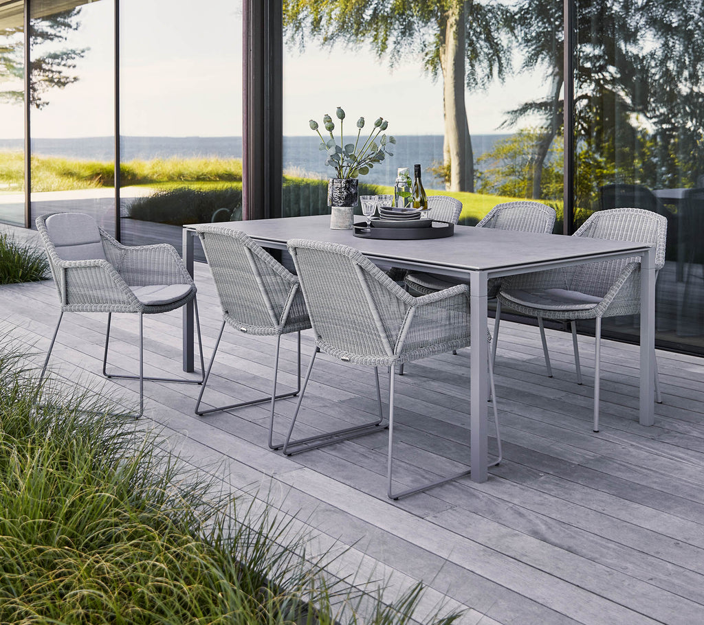 Un conjunto de comedor al aire libre elegante que cuenta con una mesa rectangular y seis sillas trenzadas, rodeado de vegetación y una vista escénica.
