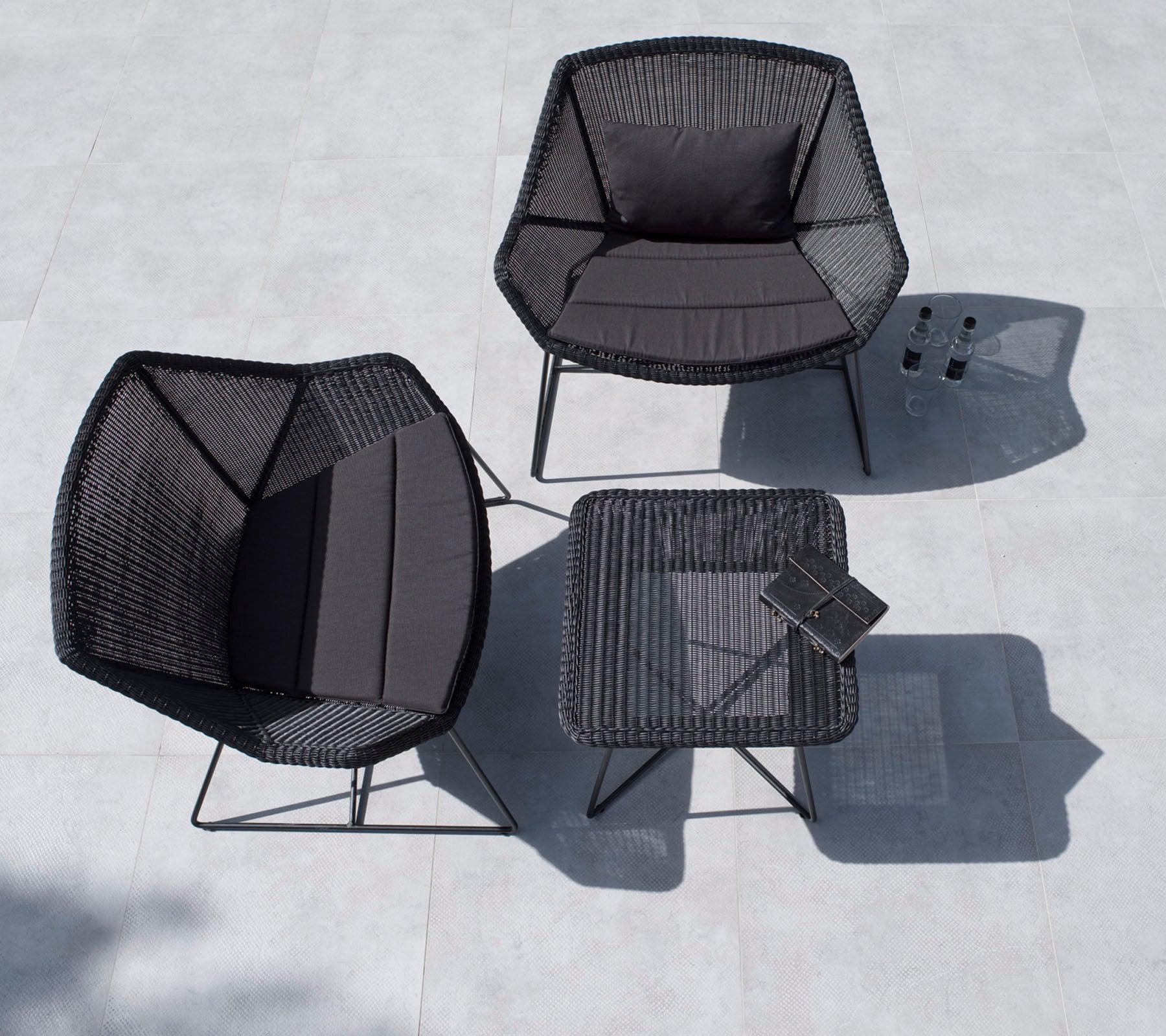 Conjunto de asientos de exterior elegante que incluye dos sillas hexagonales y una mesa cuadrada, todo en negro con un diseño minimalista.