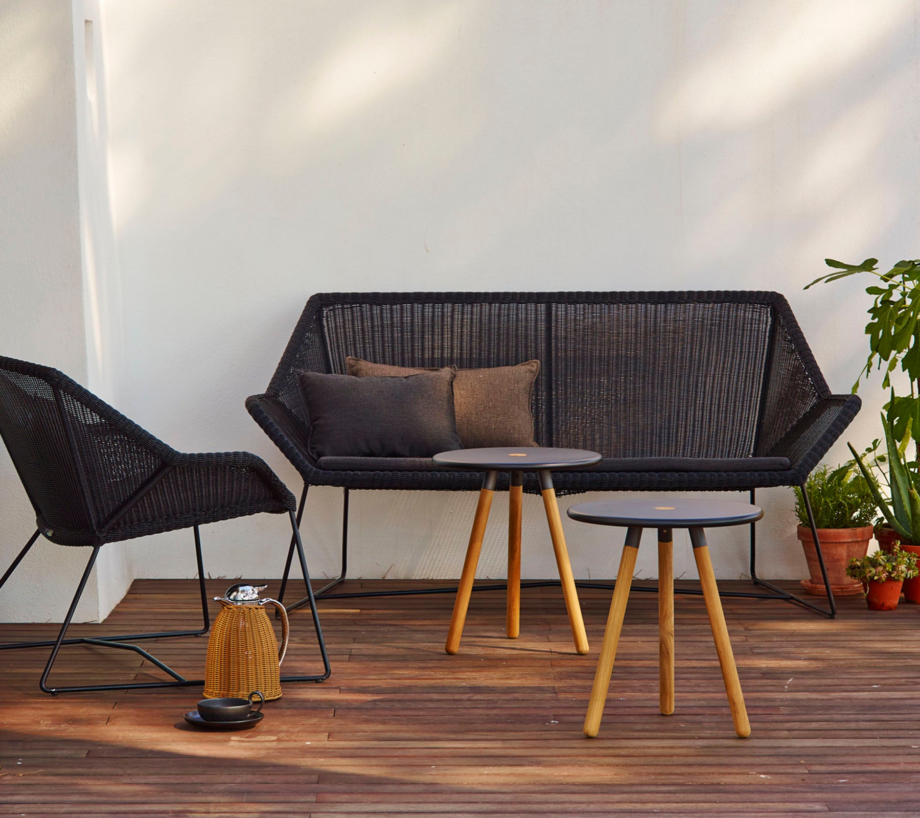 Disposición contemporánea de asientos con un sofá negro con cojines, una silla a juego y una mesa redonda con patas de madera.